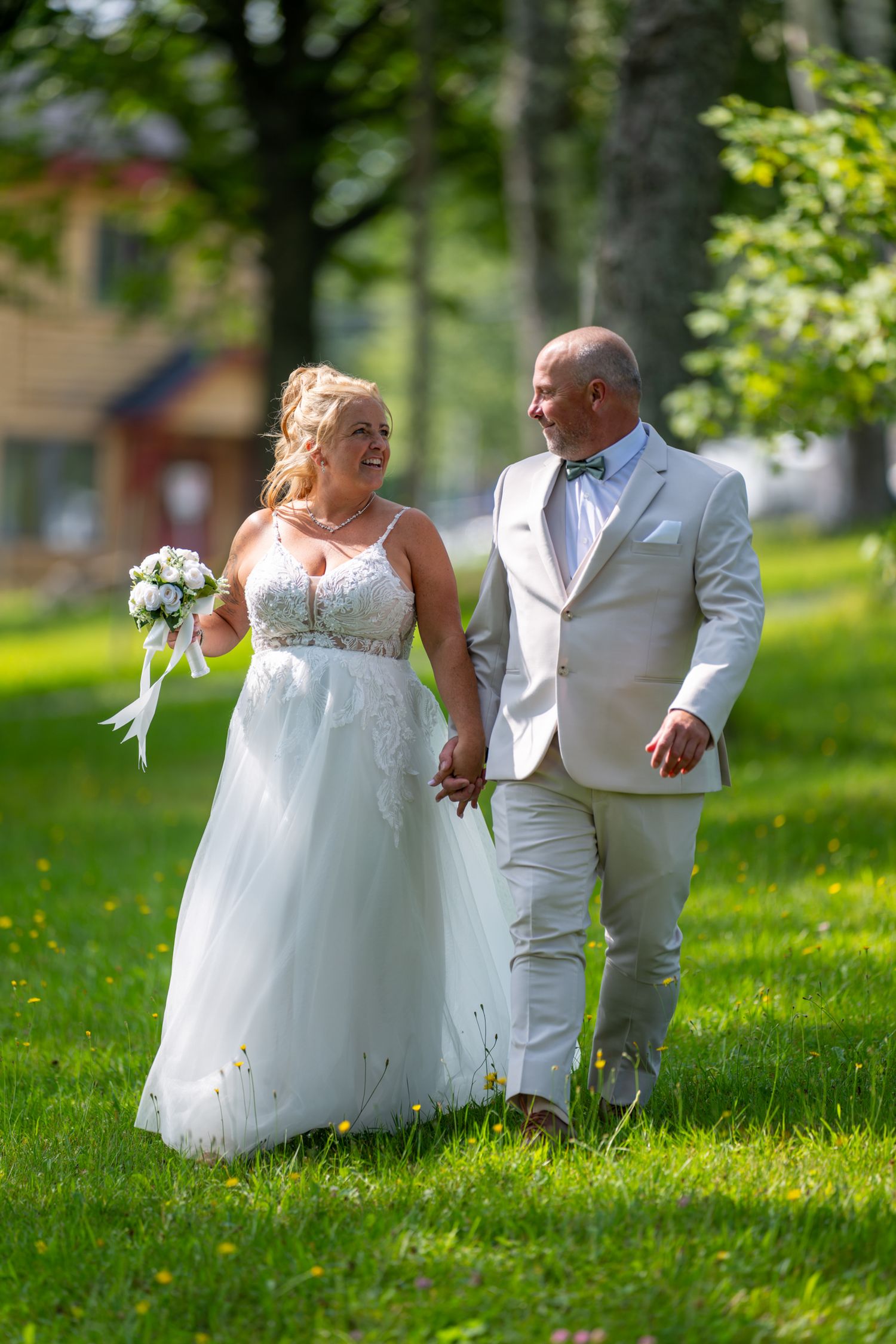 Joyful couple holding hands and walking through a lush green park during an outdoor wedding in Quebec