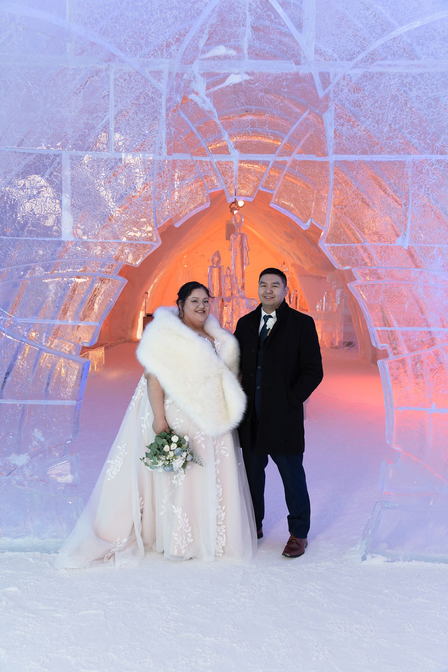 Wedding couple standing inside a glowing, sculpted ice hall at the Hôtel de Glace, Quebec City