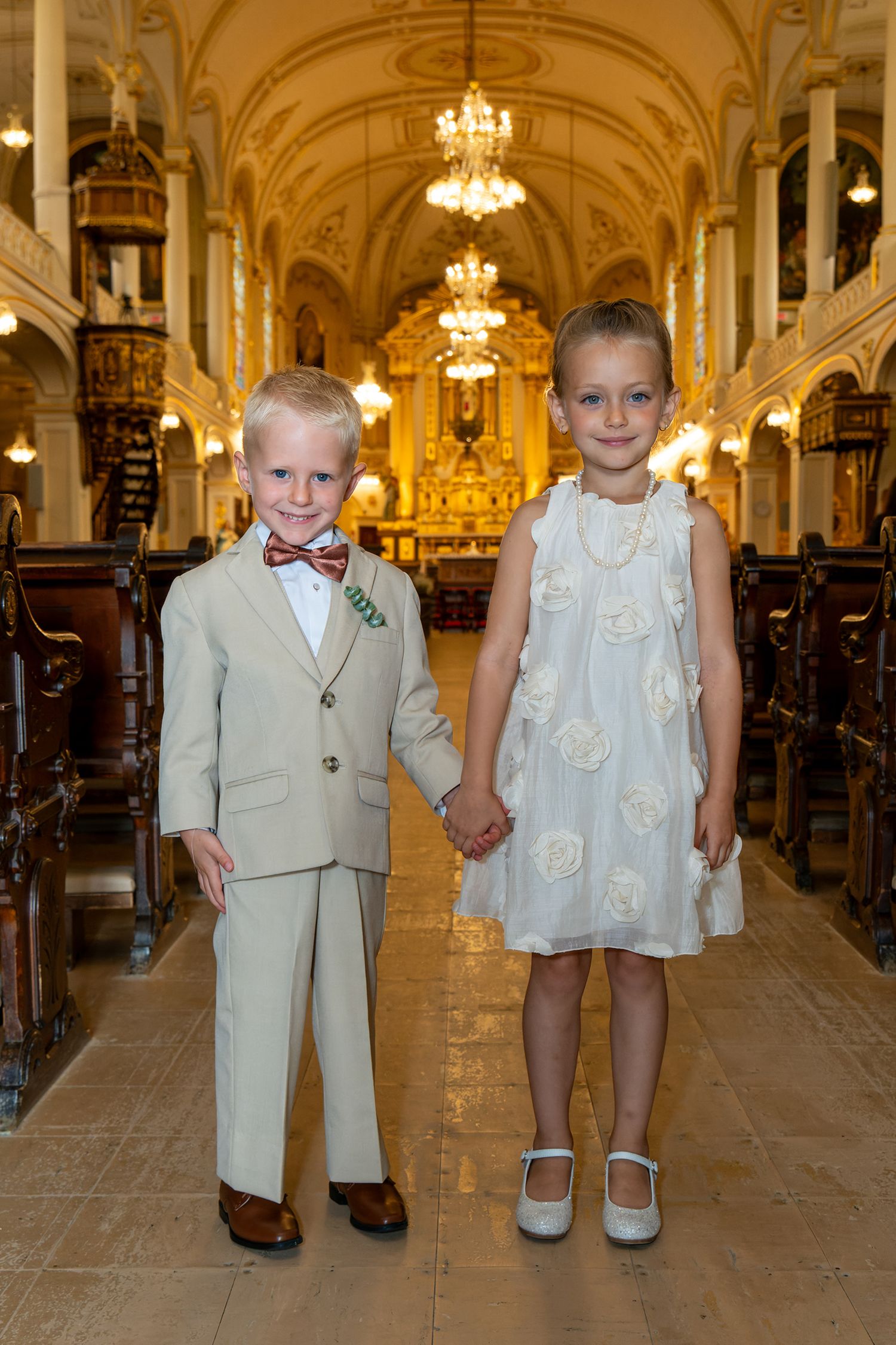 Young ring bearer and flower girl holding hands in a magnificent historic Quebec church