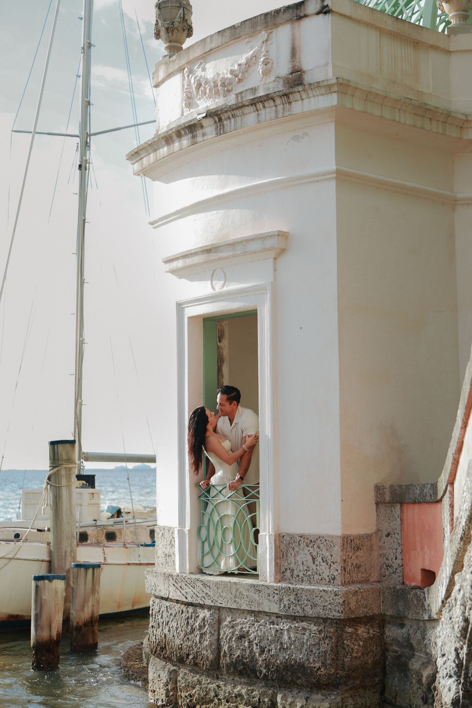 Couple sharing a romantic kiss in a waterfront white archway near sailboat.