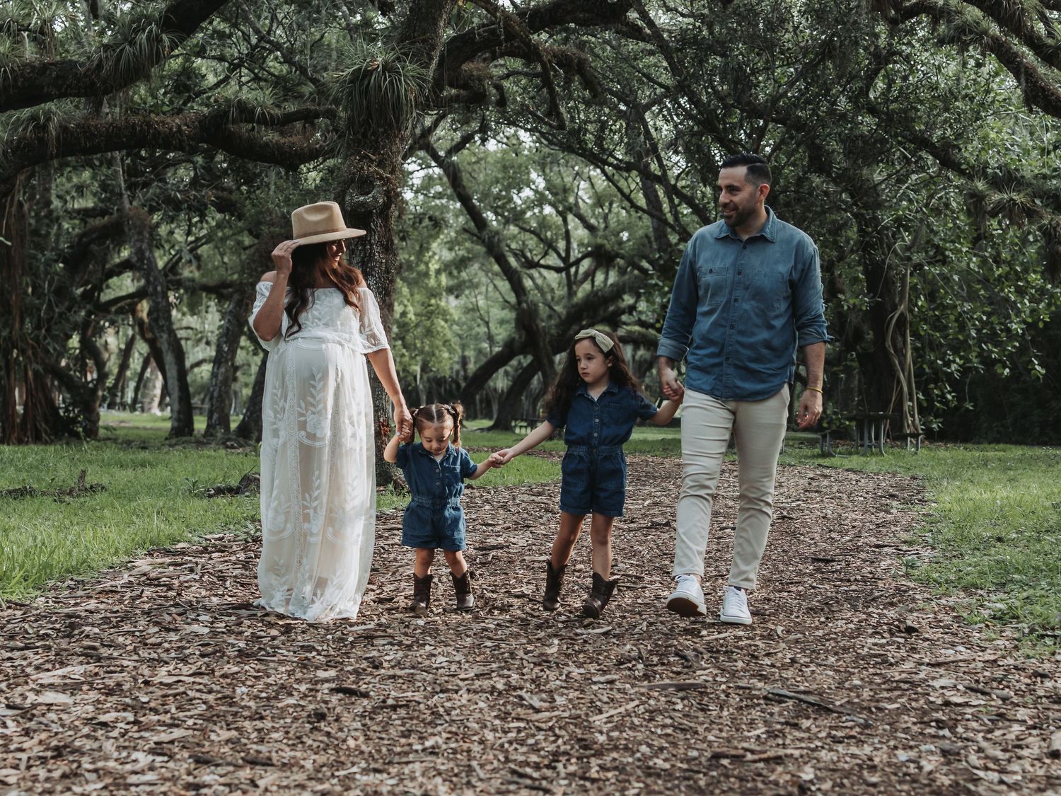 A young family of four walks together on a wooded path during a maternity photo session.
