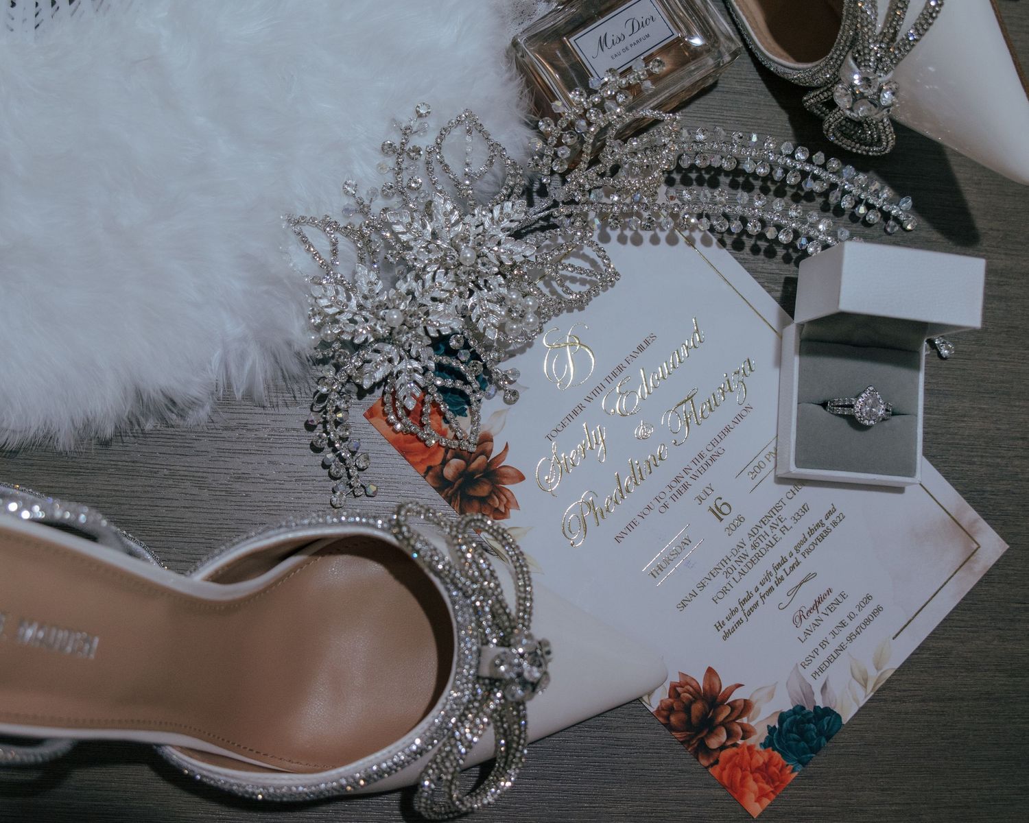 Flat lay of bridal accessories including crystal heels, diamond ring, jewelry, and a colorful wedding invitation.