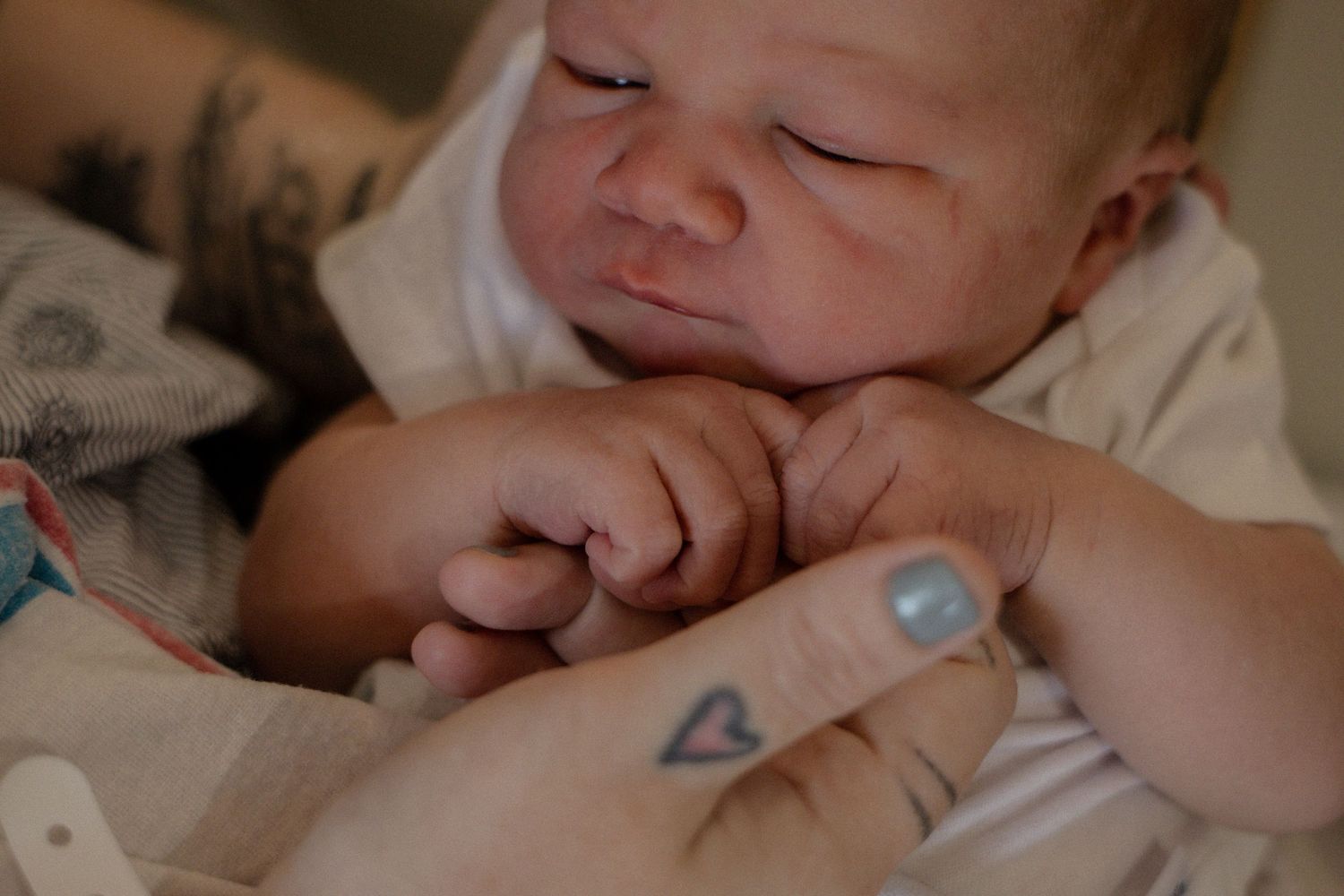 Newborn baby grasping parent's finger with small tattooed hand in tender hospital moment.