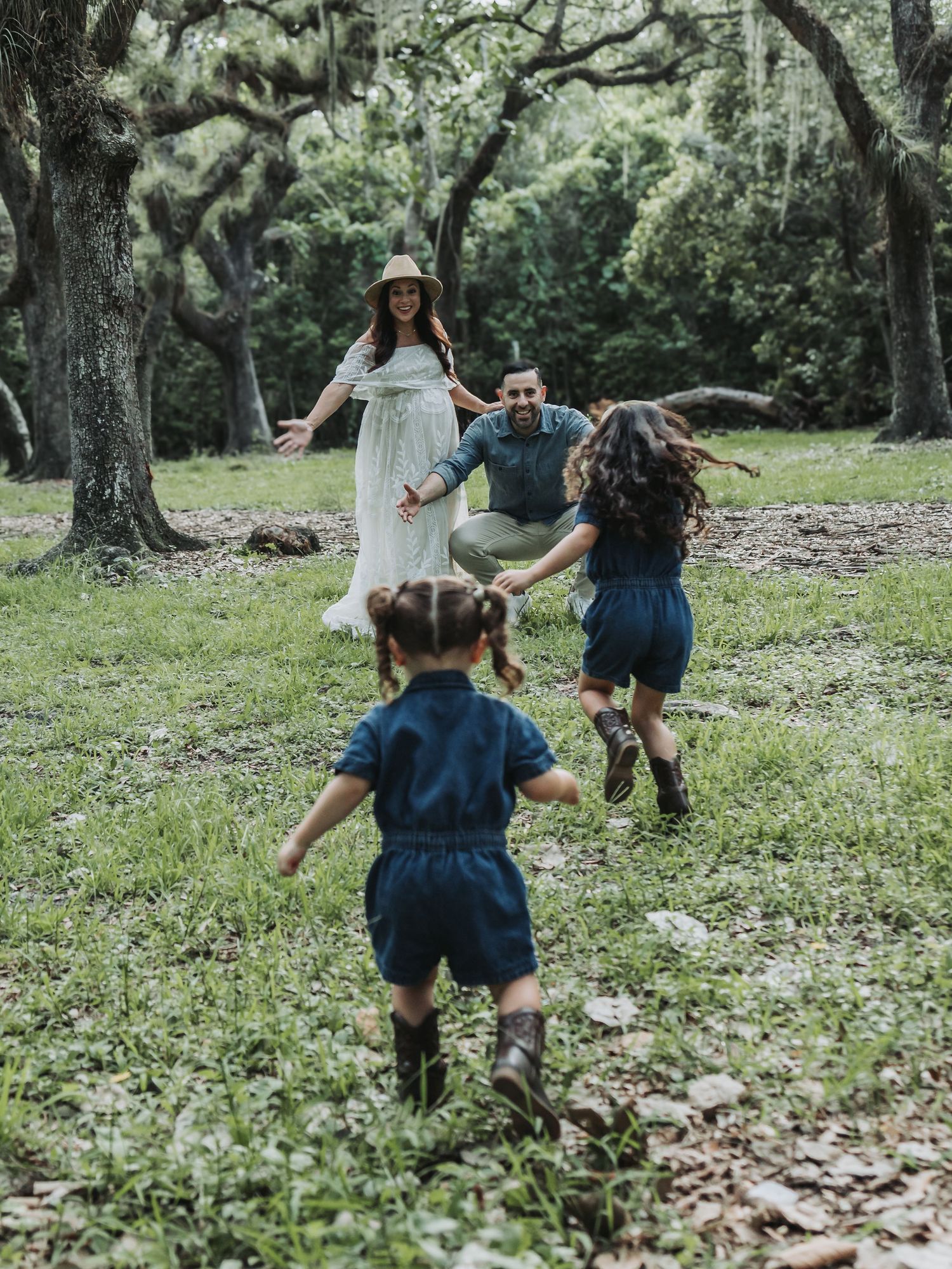 Two young children run toward their parents in a beautiful green outdoor maternity photo session.