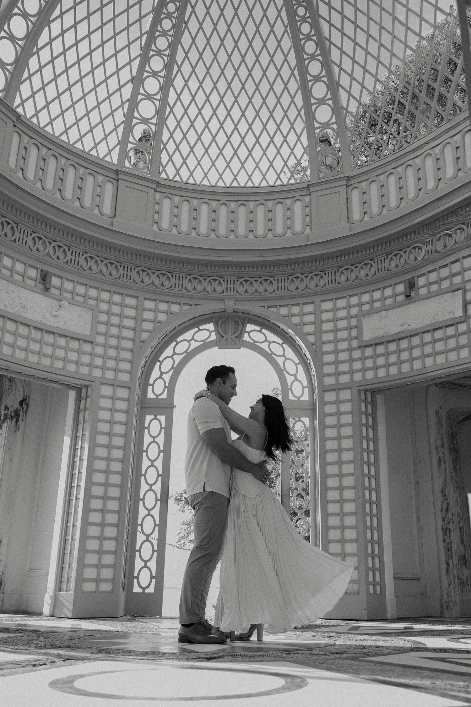 A couple dances romantically in black and white beneath an ornate domed ceiling with arched windows.