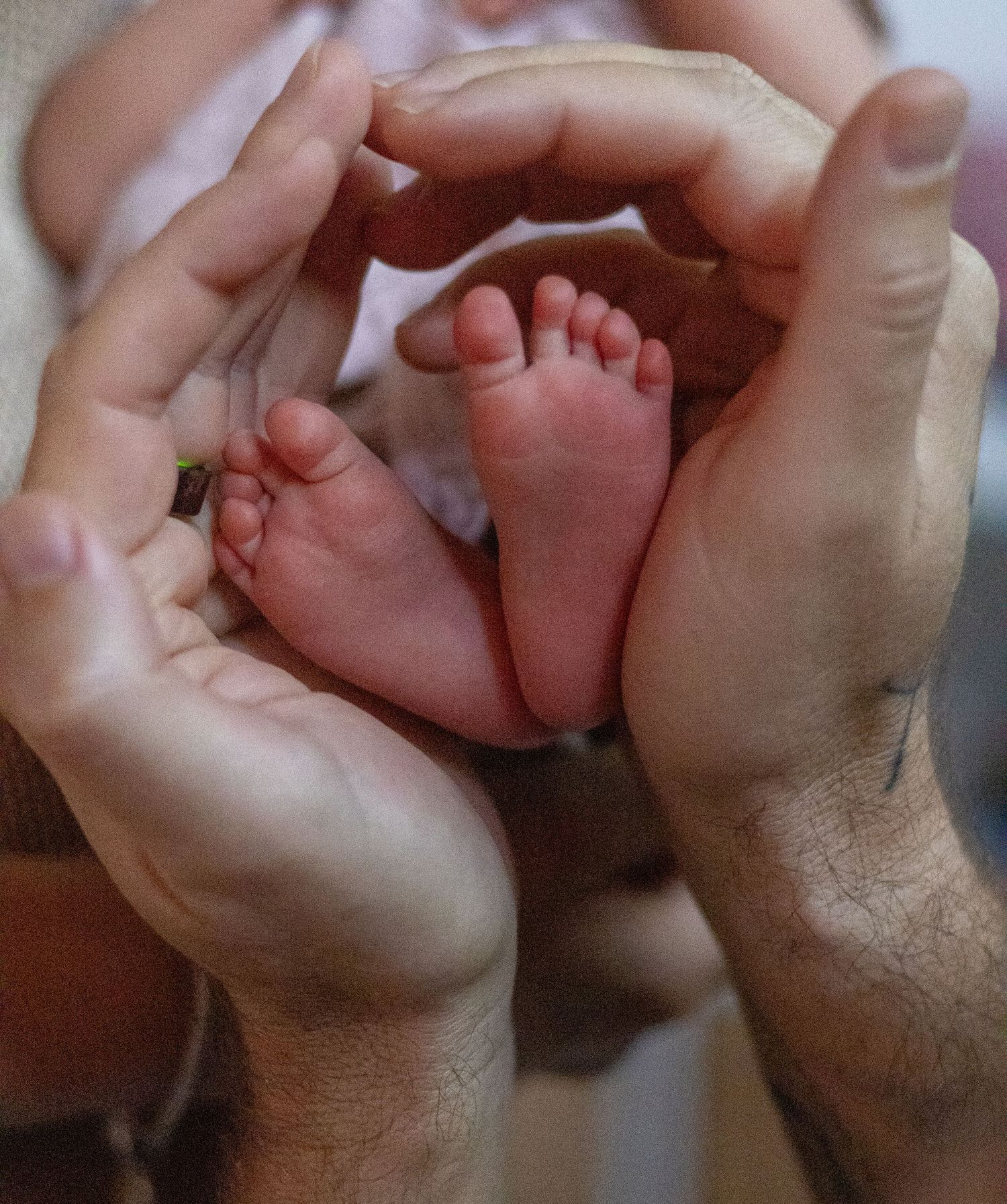 Two parents forming a heart shape with their hands around their newborn baby's tiny feet.