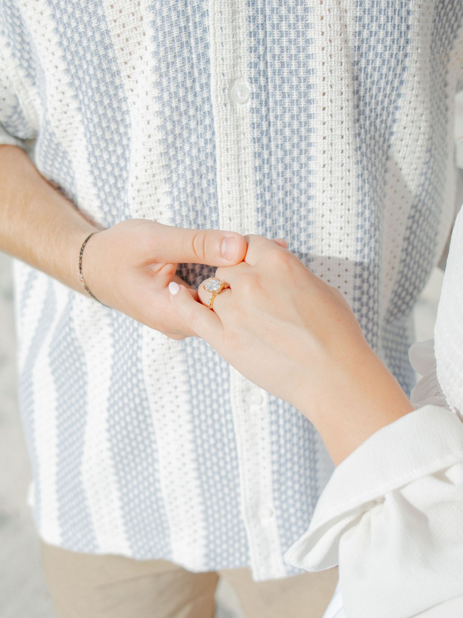 Close-up of a woman's hand wearing a gold ring gently holding a man's hand, both dressed in casual attire.