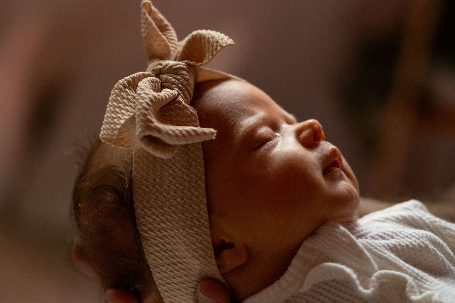 Sleeping newborn baby girl wearing an oversized beige bow headband, close-up portrait.