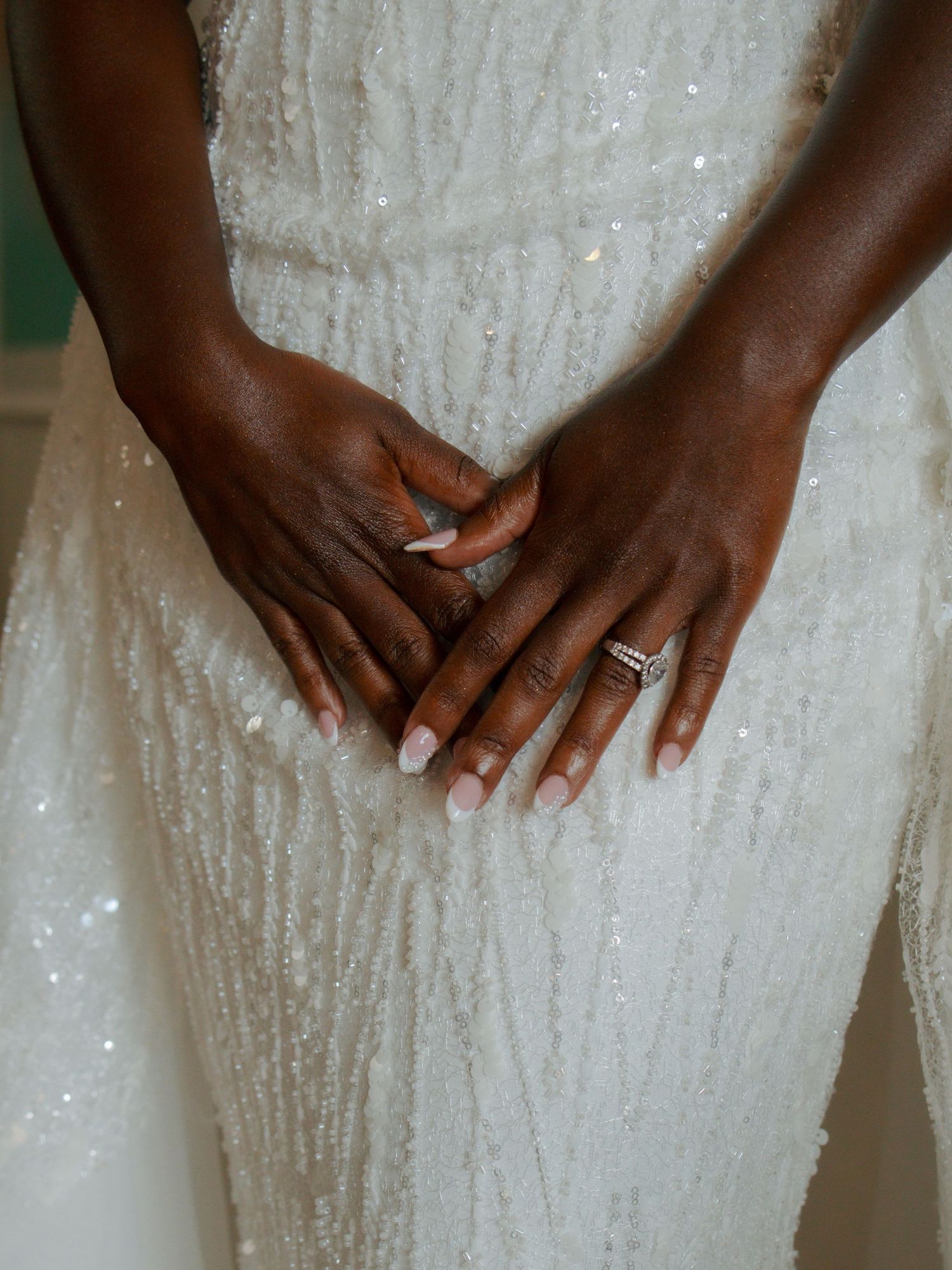 Close-up of a bride's hands showing her diamond engagement ring on a beaded white wedding gown.