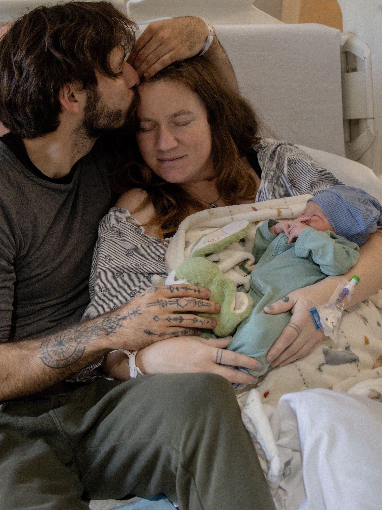 New parents sharing tender moment with newborn baby in hospital bed after delivery.