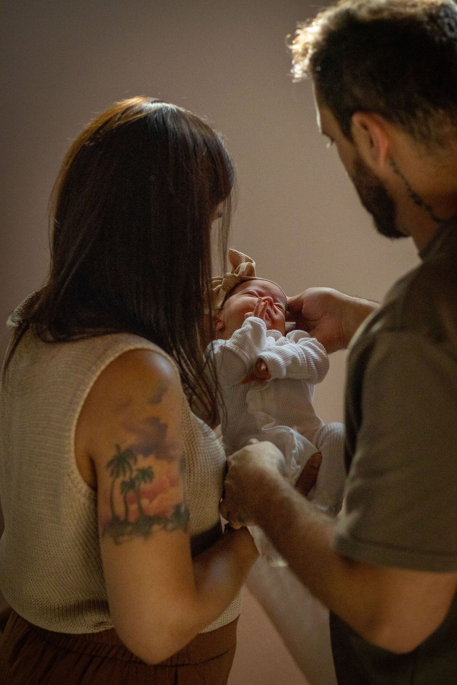 New parents standing together admiring their swaddled newborn baby in a warm light.