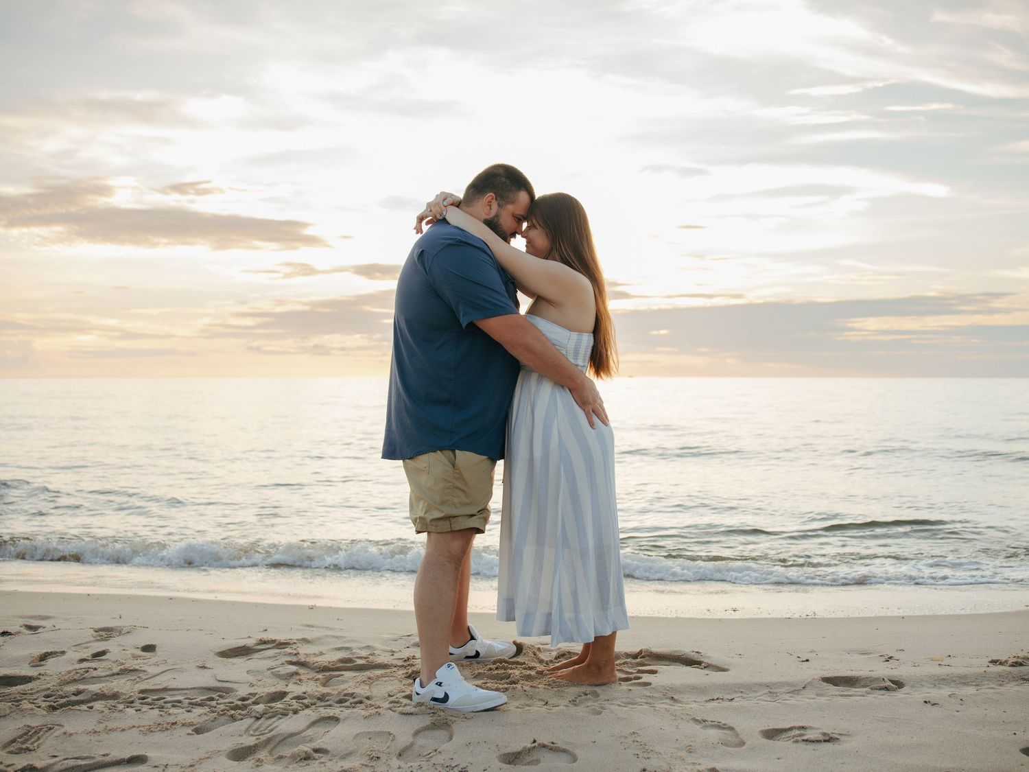 Couple sharing a tender embrace on a sandy beach during a golden sunset by the ocean.