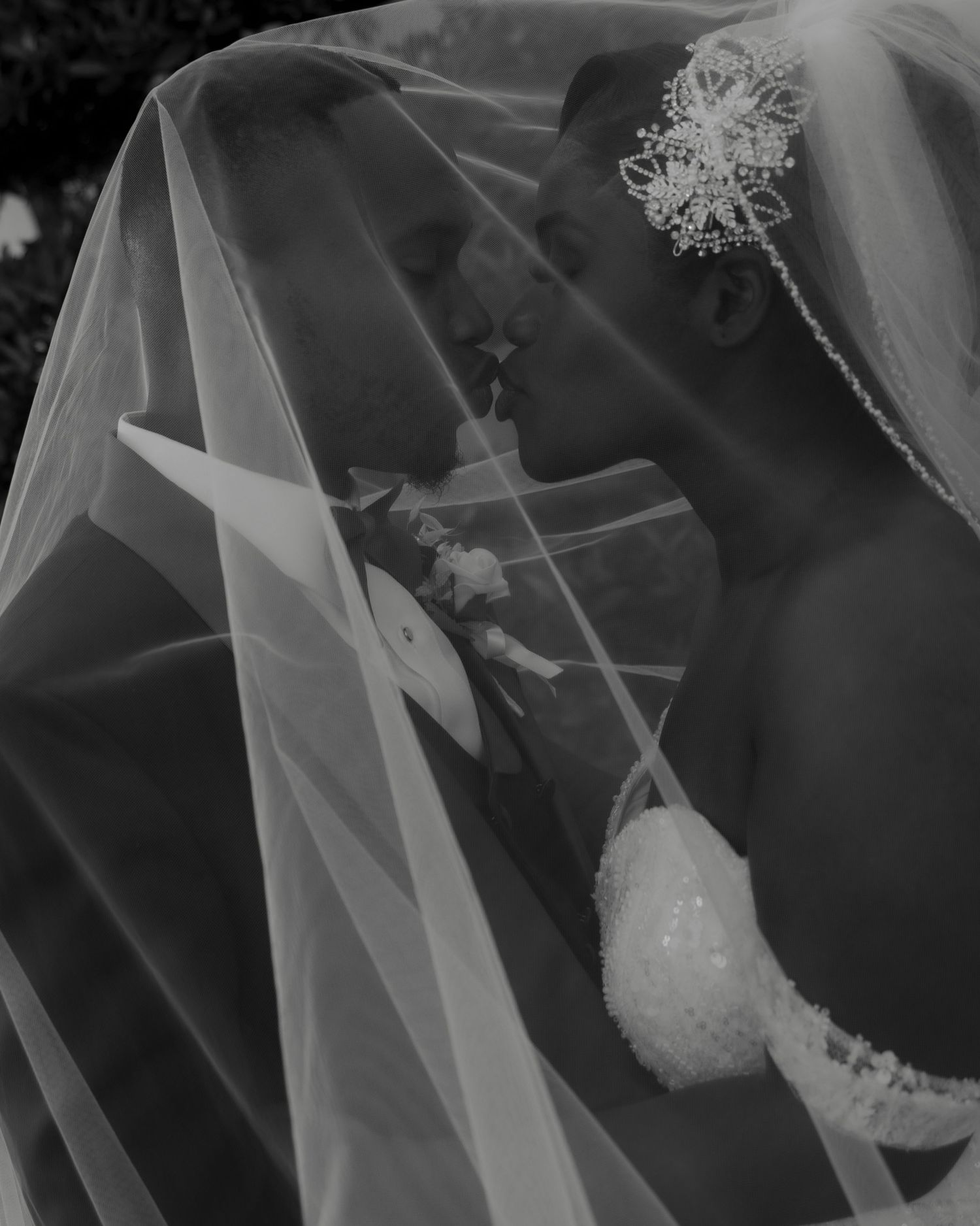 Black and white wedding photo of bride and groom kissing under flowing bridal veil.