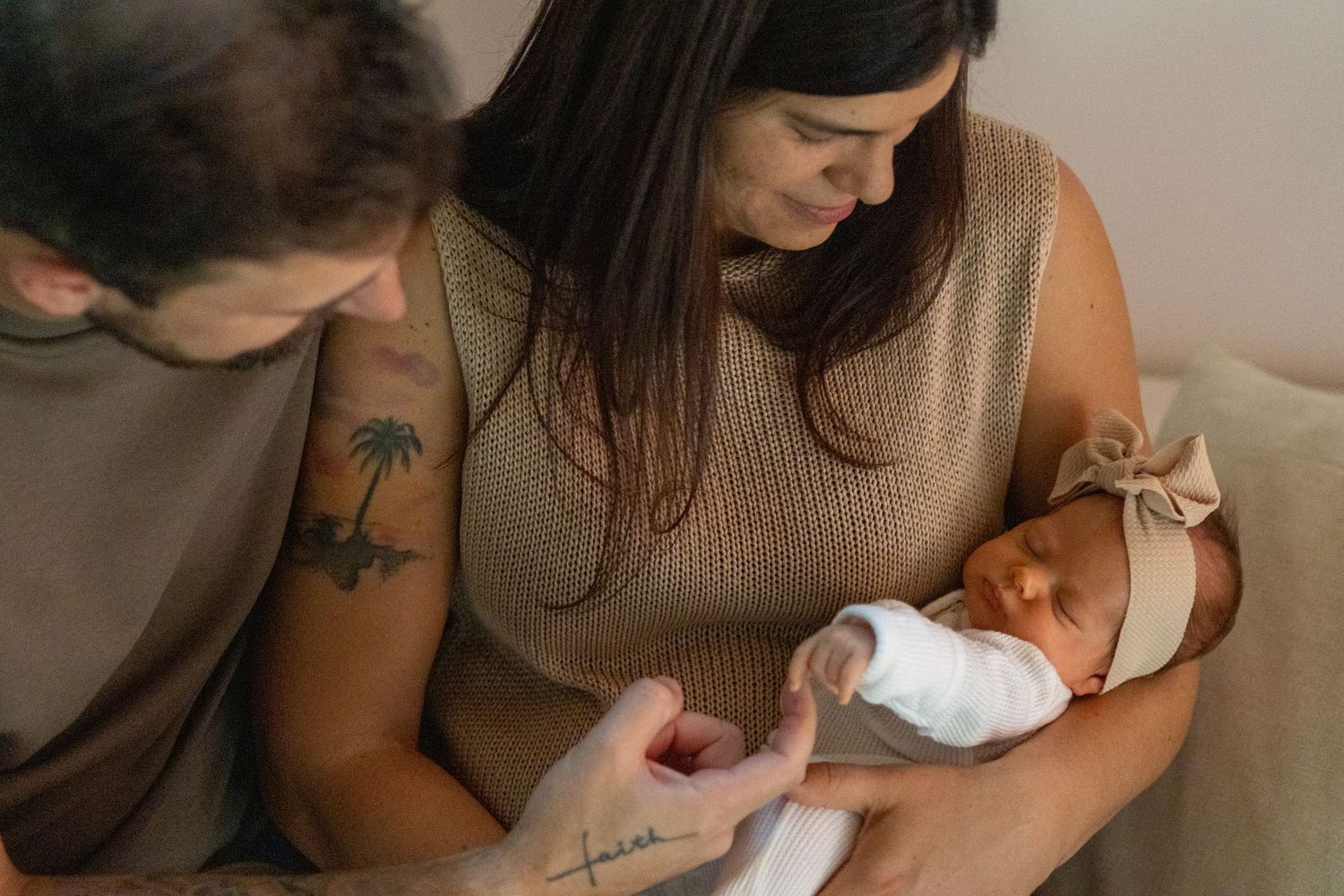 New parents lovingly holding their swaddled newborn baby girl with bow headband.
