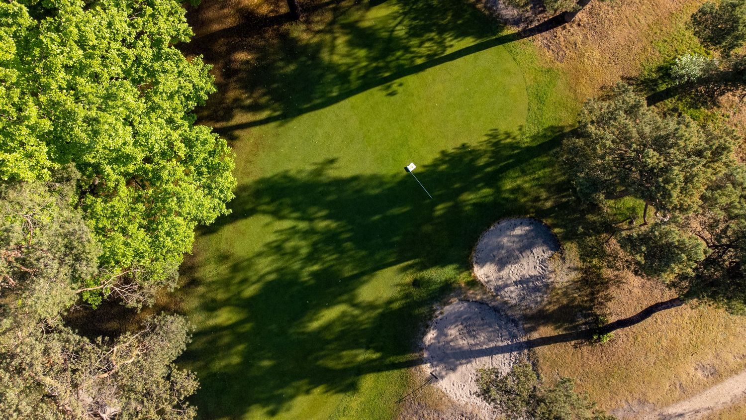 Aerial view of a golf course fairway surrounded by trees casting long shadows.