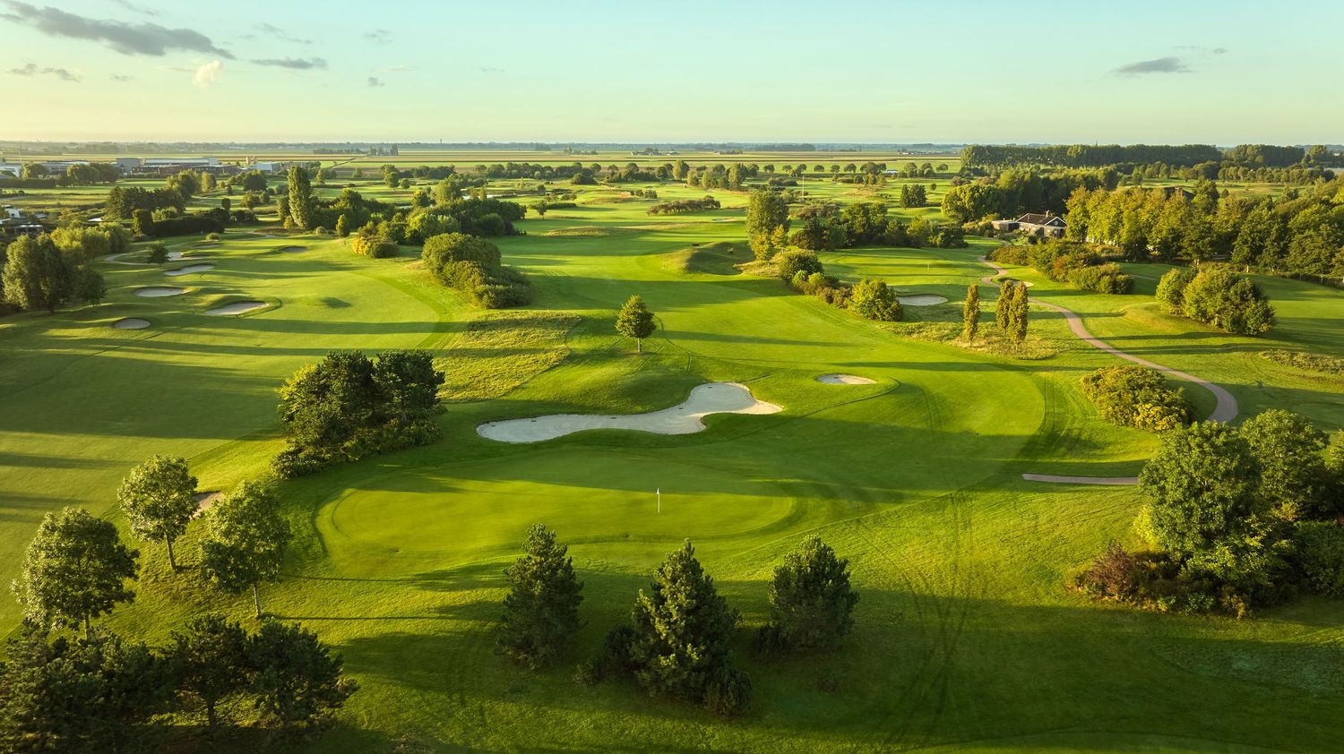 Aerial view of a scenic golf course featuring manicured fairways, sand bunkers, and tree-lined greens at golden hour.