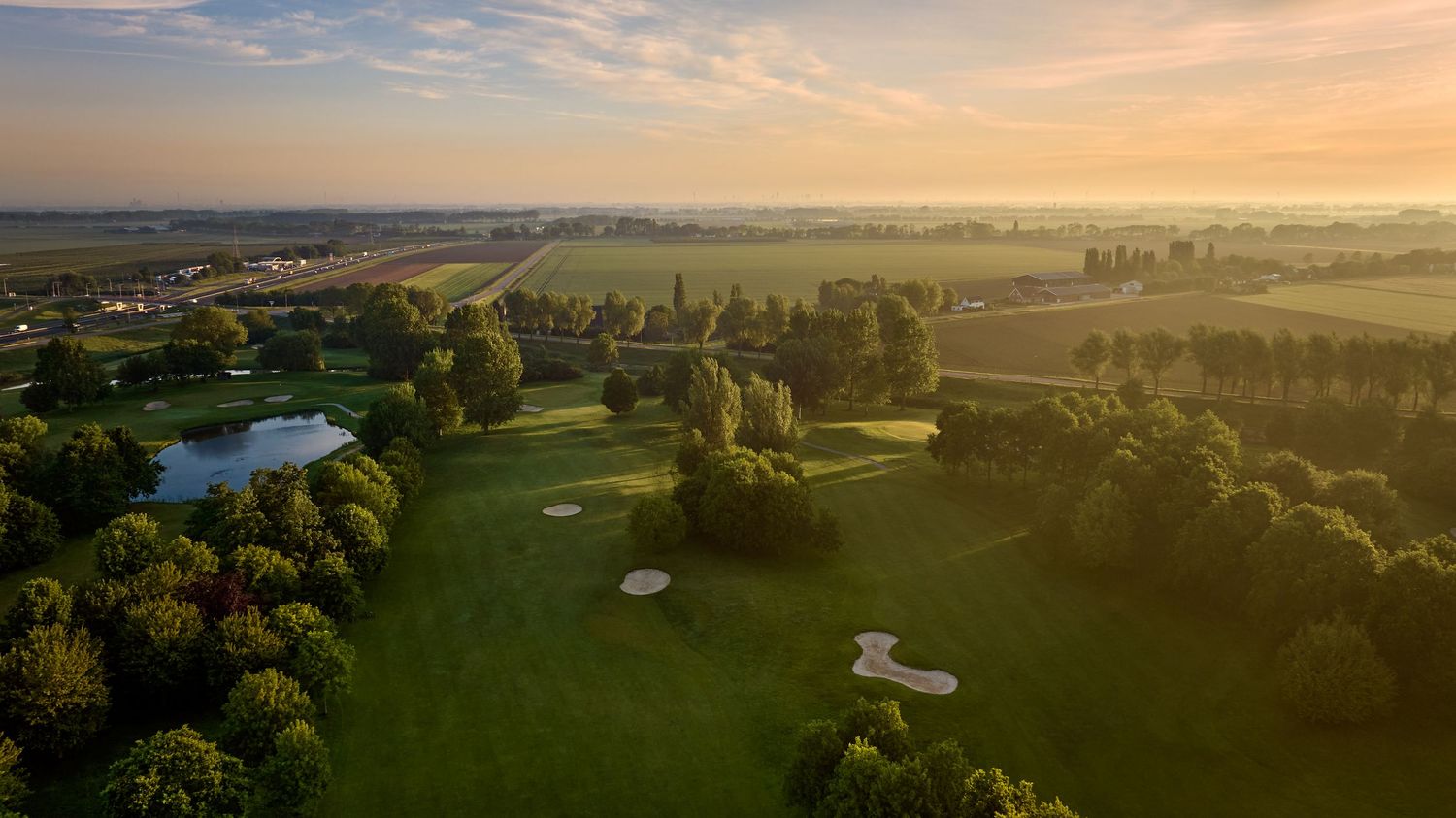 Aerial sunrise view of a golf course with sand bunkers, ponds, and rolling green fairways.
