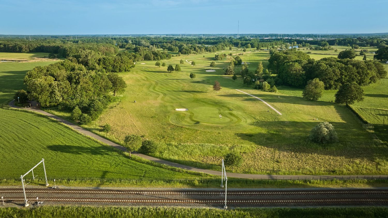 Aerial view of a golf course with sand bunkers beside a rural road and open fields.