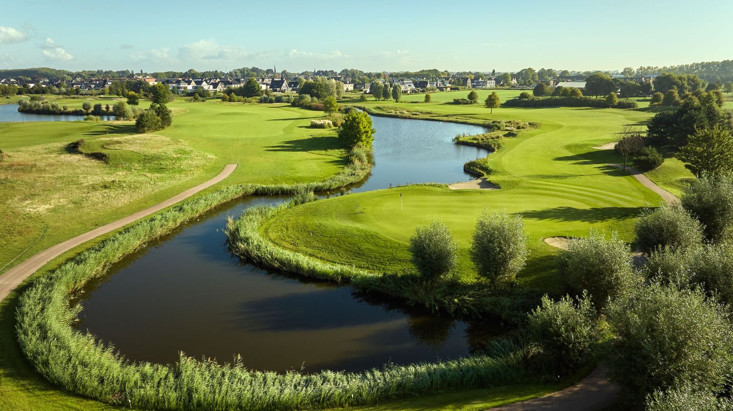 Aerial view of a golf course with winding water features, lush fairways, and a residential area in the background.