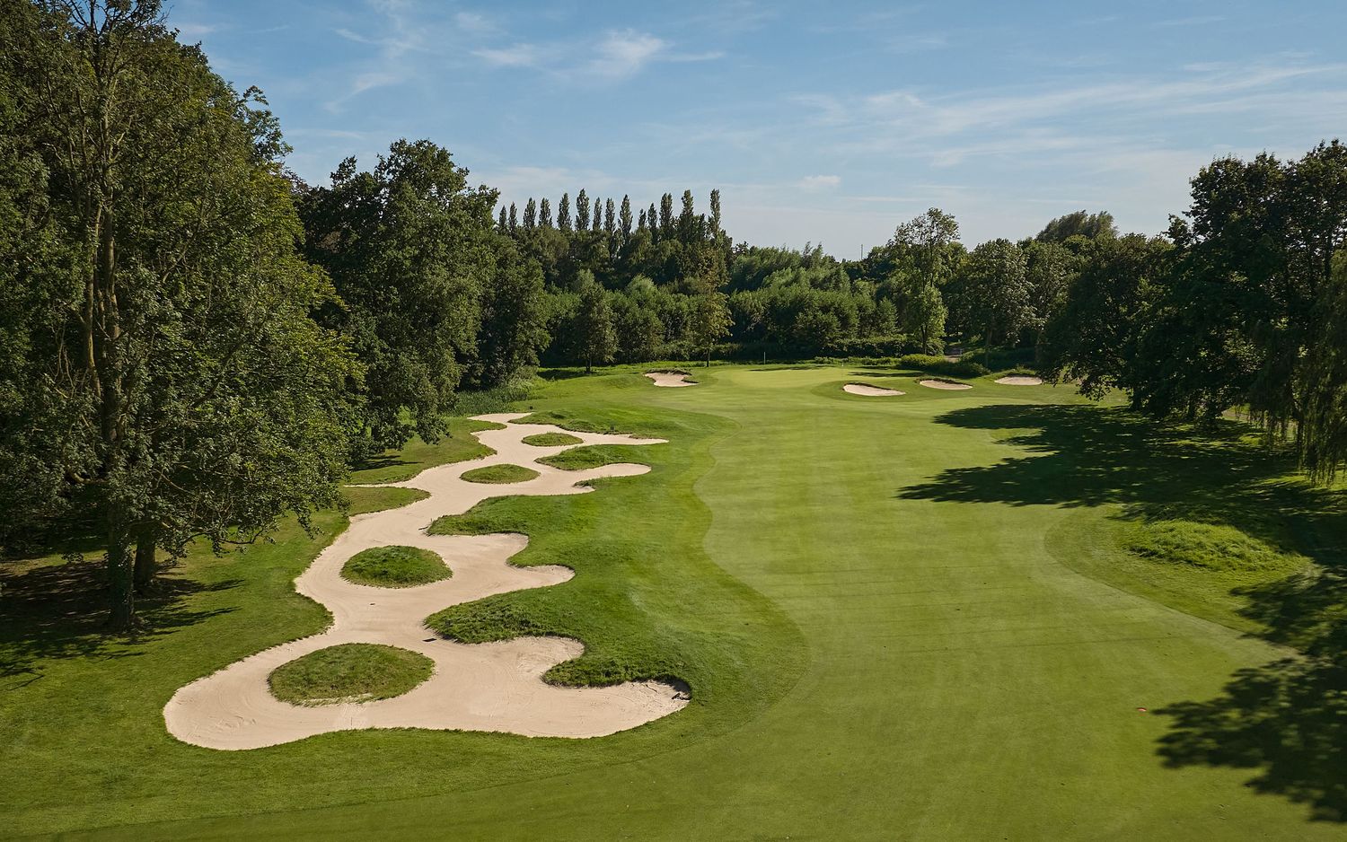 Aerial view of a lush golf course fairway lined with trees and large sand bunkers on a sunny day.