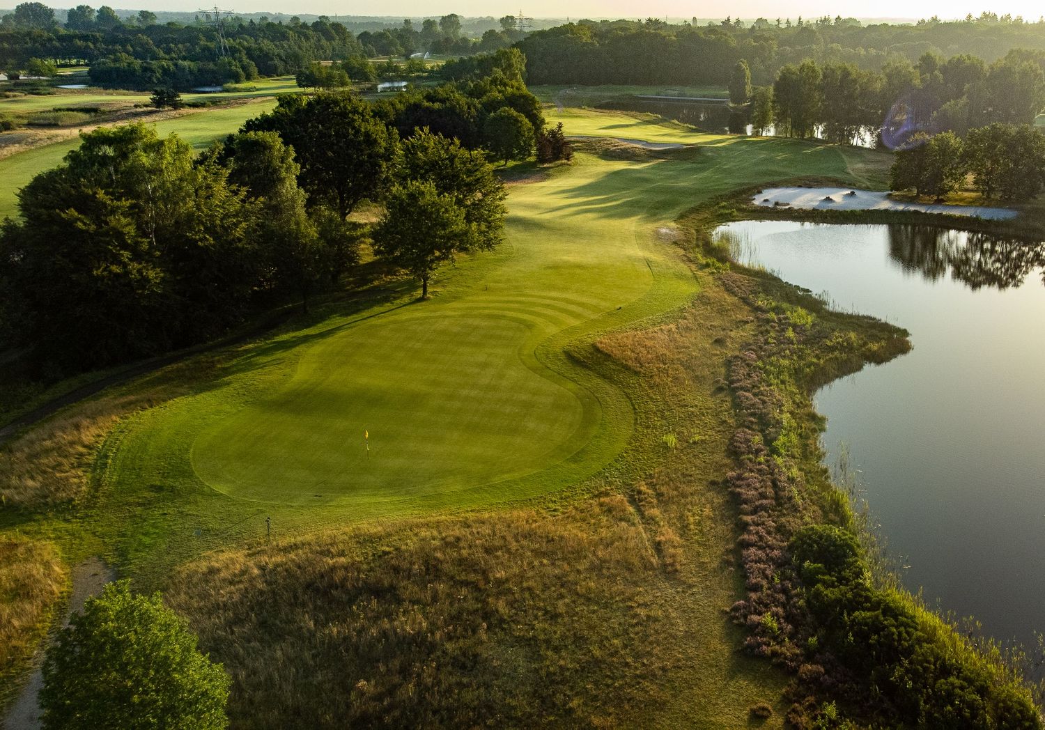 Aerial view of a golf course fairway with bunkers and a serene lake at golden hour.