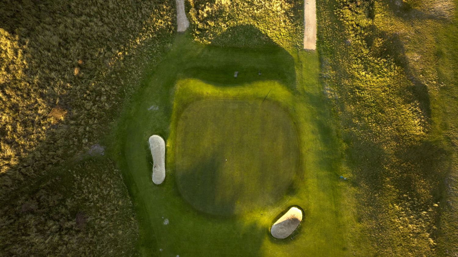 Aerial top-down view of a golf course green with two white sand bunkers surrounded by rough.