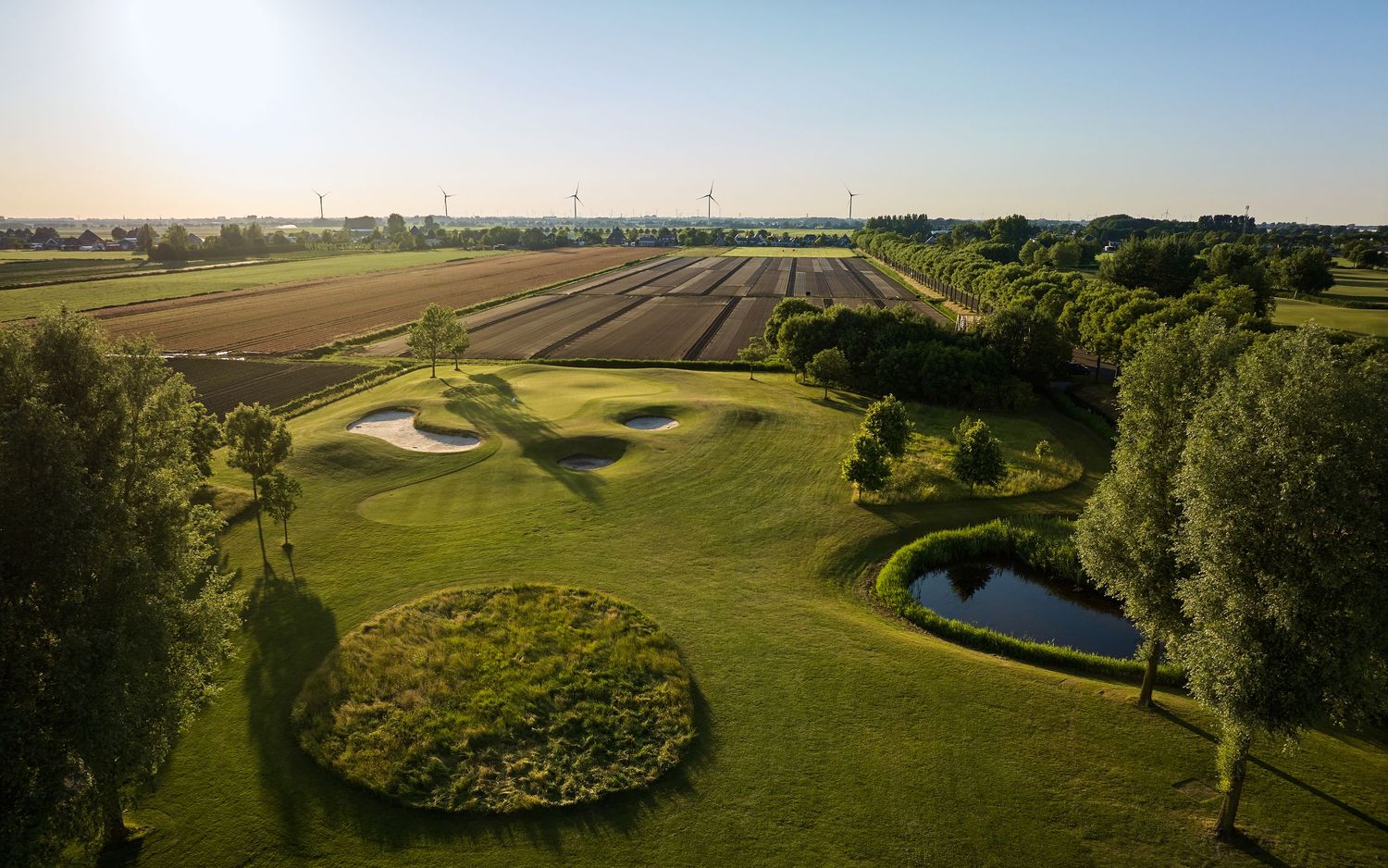 Aerial view of a golf course with bunkers and pond beside open agricultural fields.