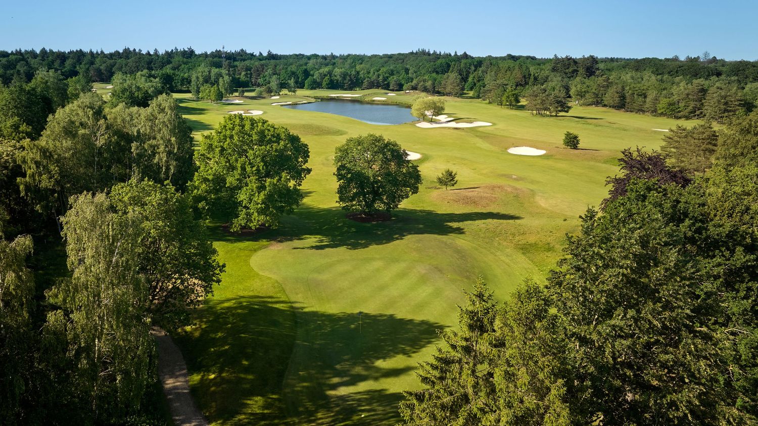 Aerial view of a golf course fairway with a pond and dense surrounding forest.