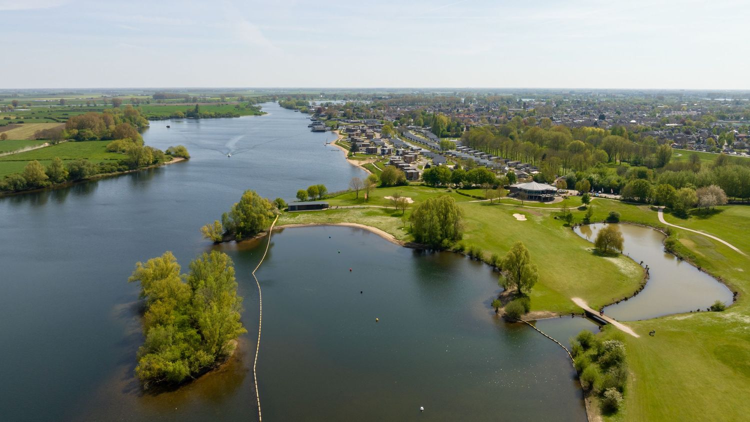 Aerial view of a golf course beside a large lake with a clubhouse and town in the background.