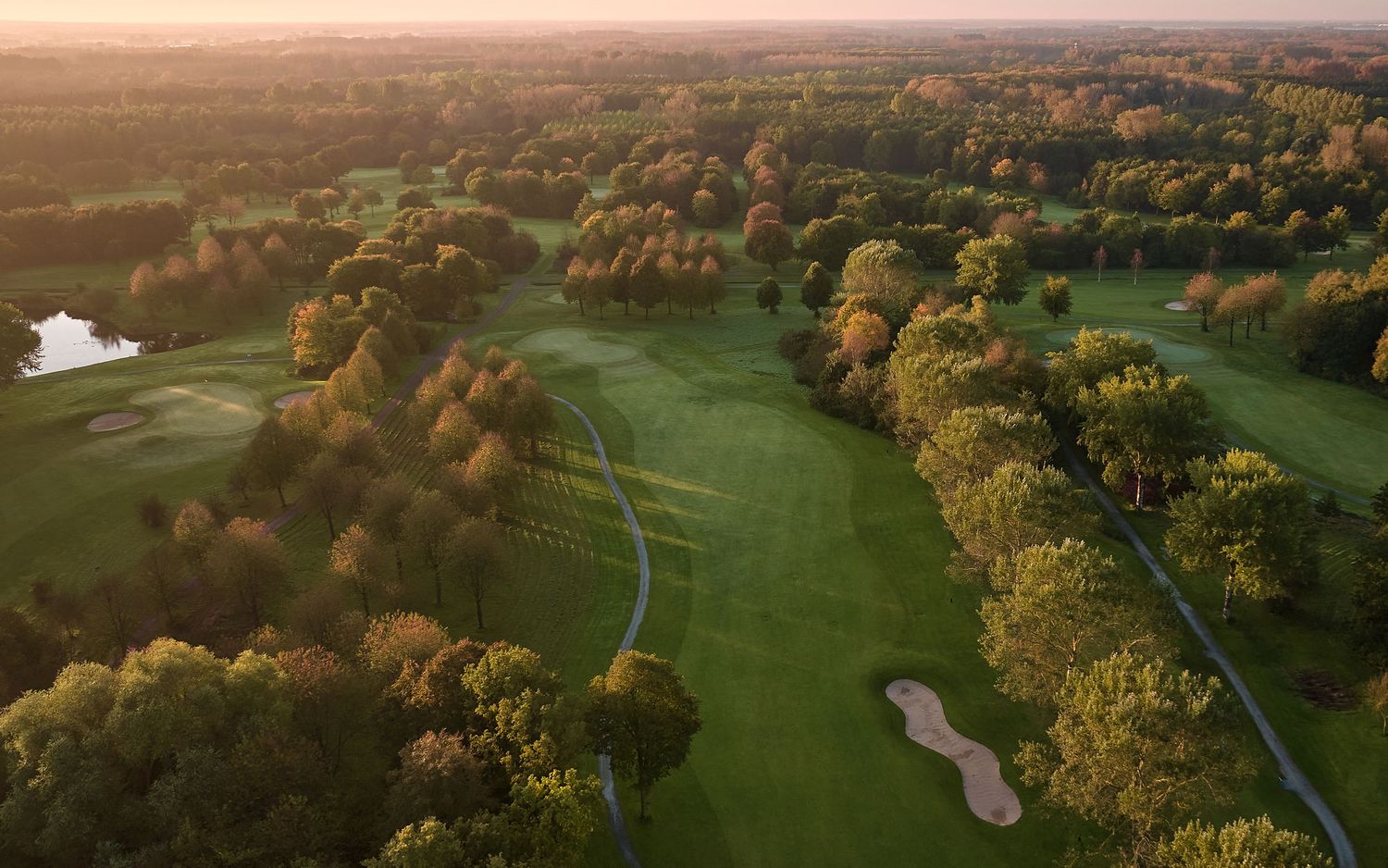 Aerial sunset view of a golf course with sand bunkers and colorful autumn foliage.
