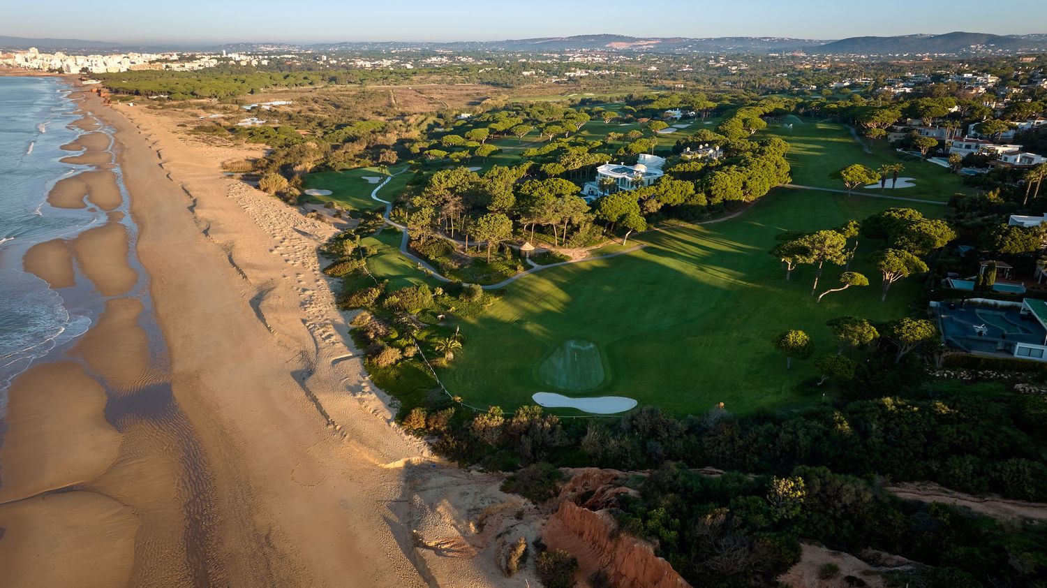 Aerial view of a seaside golf course with lush fairways stretching along a wide sandy beach in Portugal.