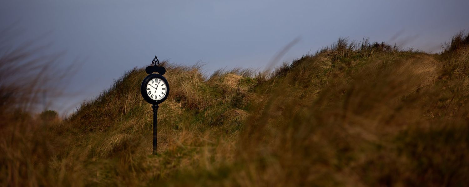 Vintage clock on a post standing among grassy sand dunes on a links golf course under moody skies.