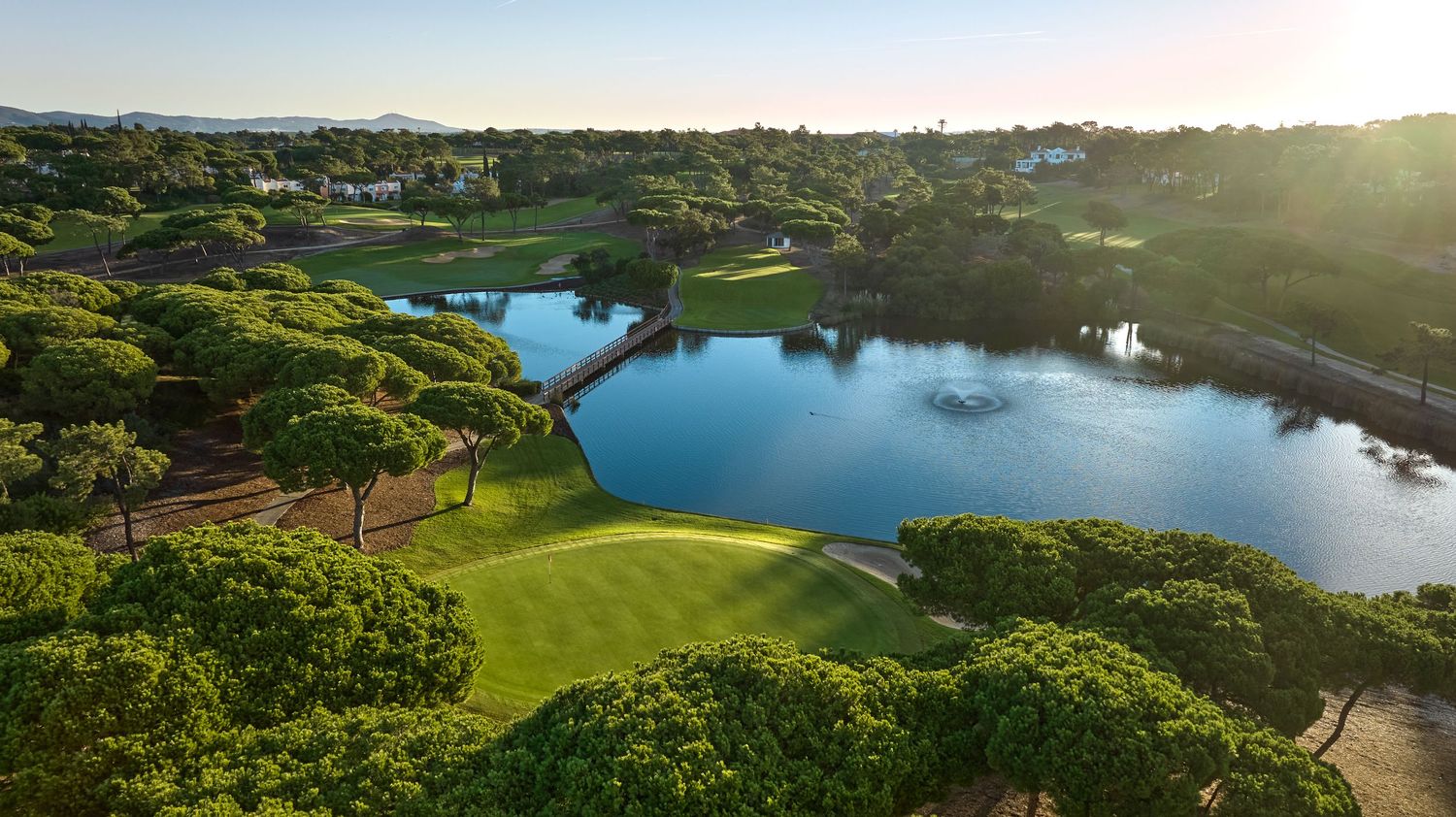 Aerial view of a verdant golf course with a scenic lake surrounded by pine trees in the Algarve, Portugal.