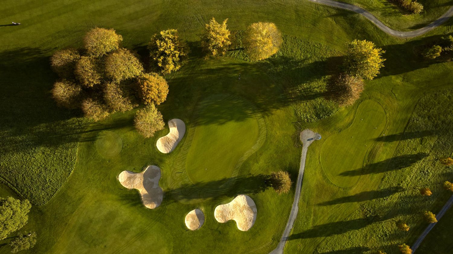 Aerial view of sunlit golf course fairway with multiple sand bunkers and tree-lined borders.