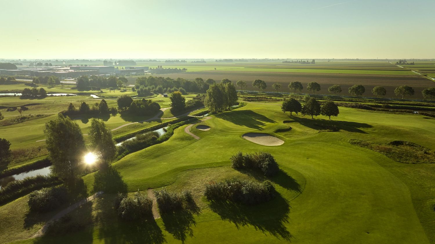 Aerial view of a flat golf course with sand bunkers, water hazards, and open countryside stretching to the horizon.