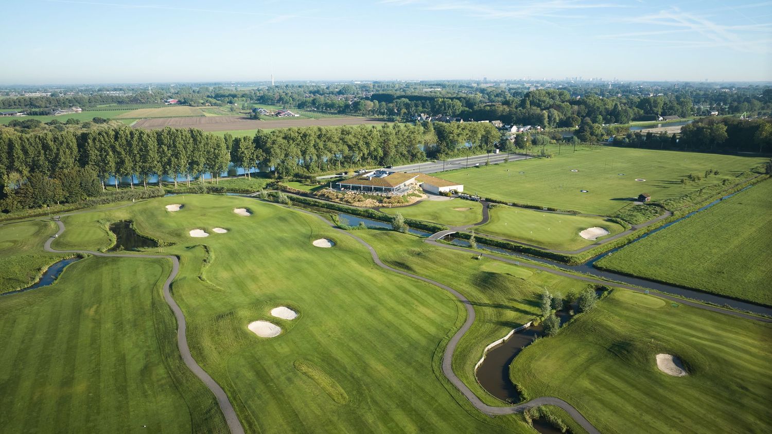 Aerial view of a flat golf course with sand bunkers, water features, and surrounding farmland.