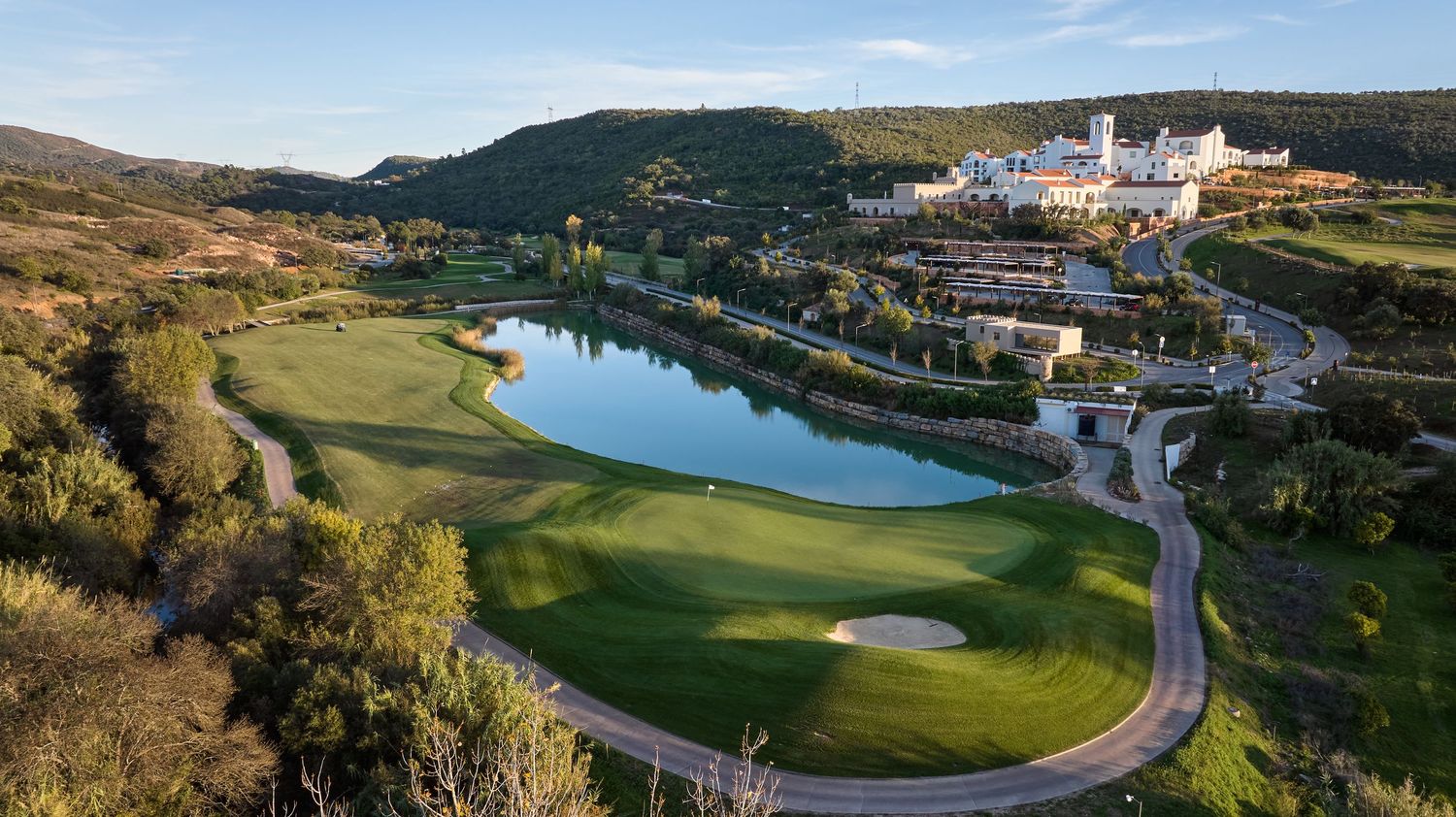 Aerial view of a resort golf course with a scenic lake, white hotel buildings, and lush greenery.