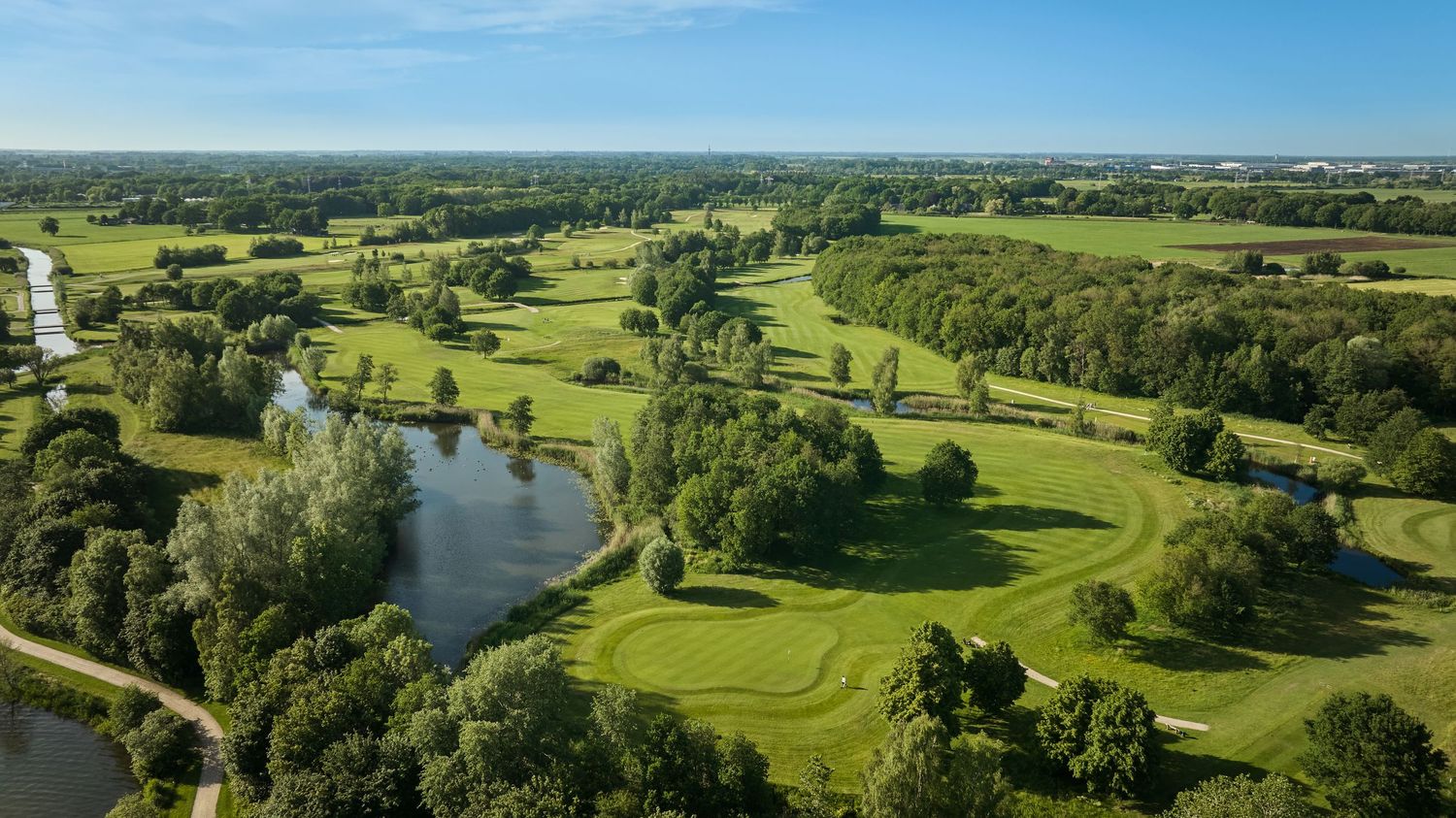 Aerial view of a scenic golf course with ponds, green fairways, and surrounding trees.