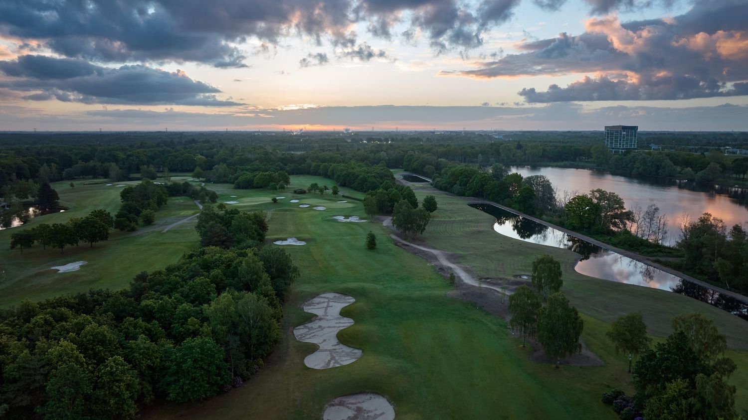Aerial dusk view of a golf course with multiple bunkers beside a calm river.
