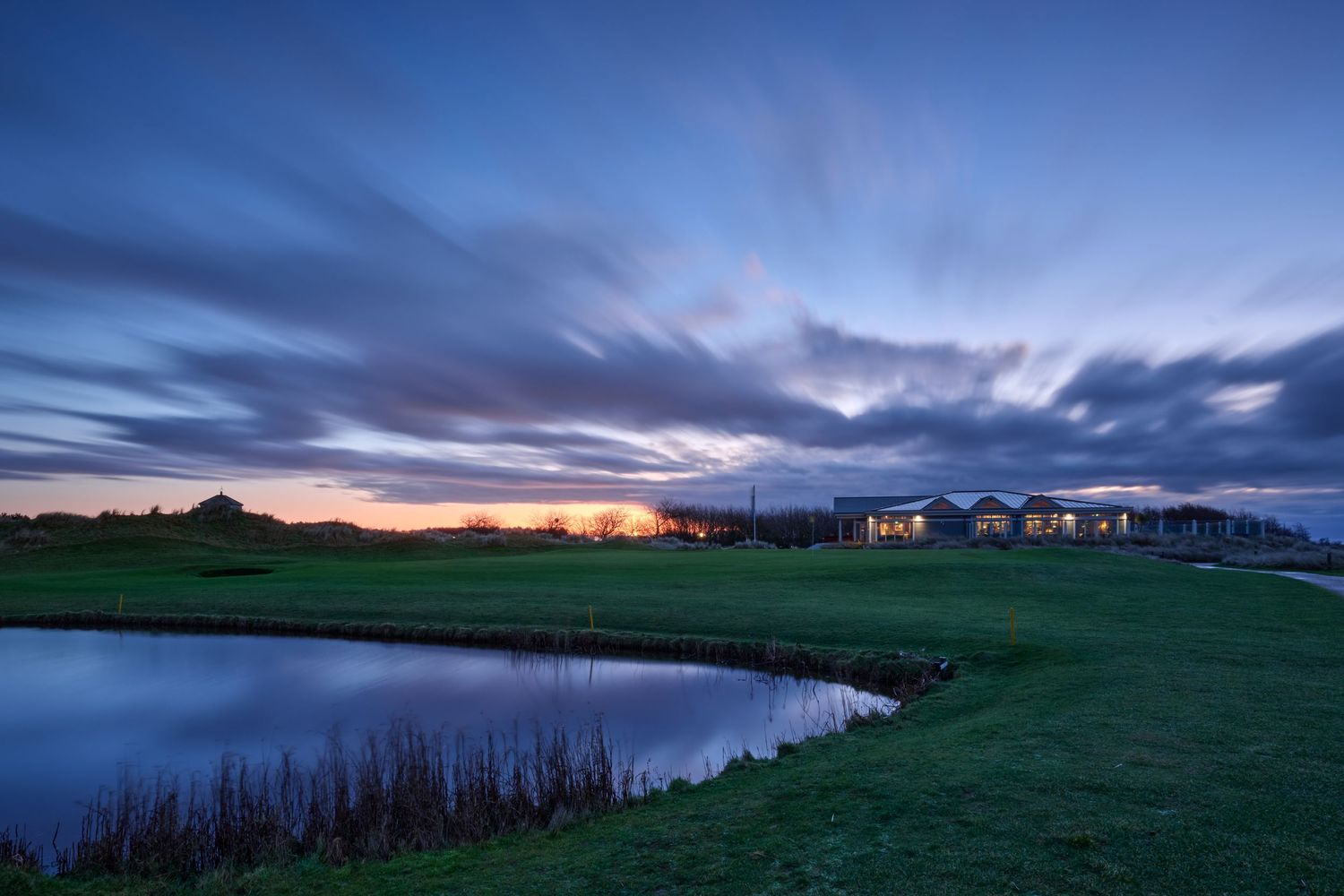 Scenic golf course at twilight with pond reflection, green fairway, and dramatic cloudy sky.