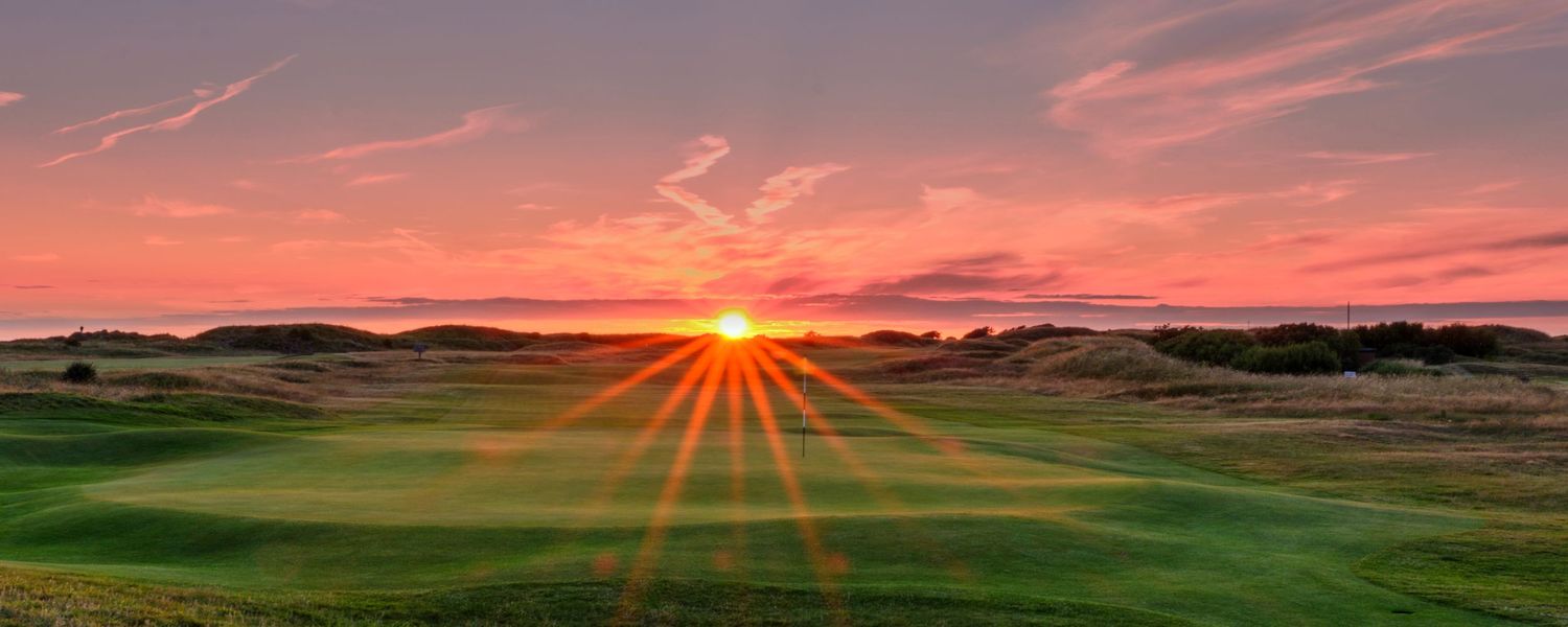 Stunning sunburst sunset over a links golf course with vibrant red and orange sky above the fairway.