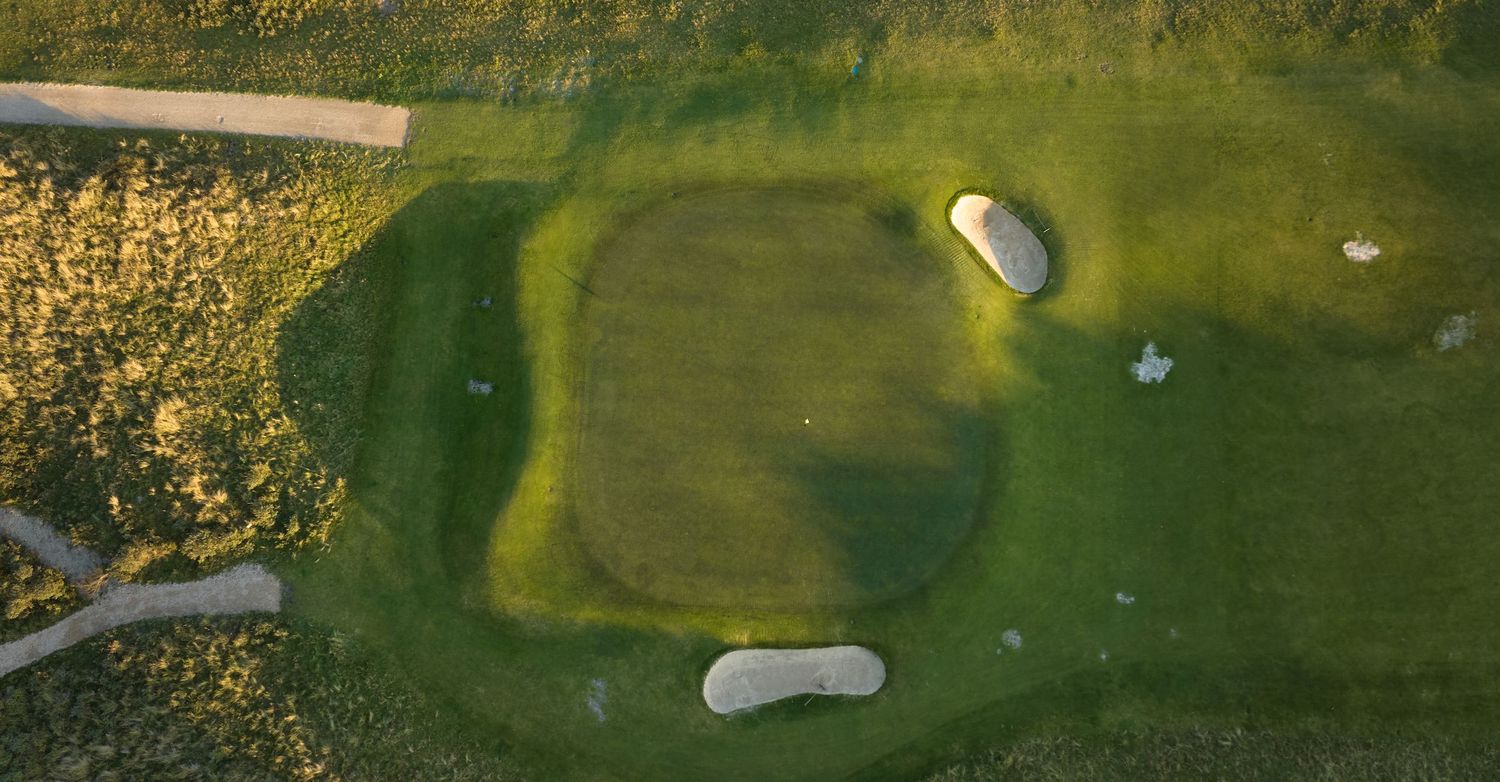 Aerial view of golf course green with two sand bunkers surrounded by golden grass at sunset.