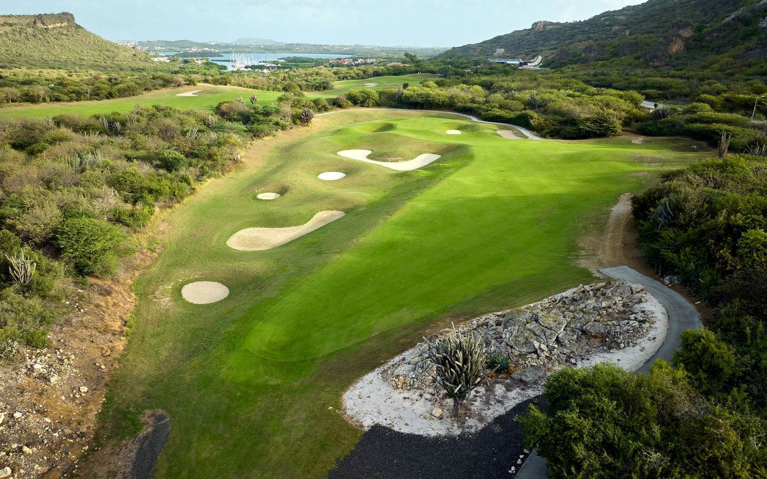 Aerial view of a scenic golf course with sand bunkers surrounded by rugged terrain and ocean views.