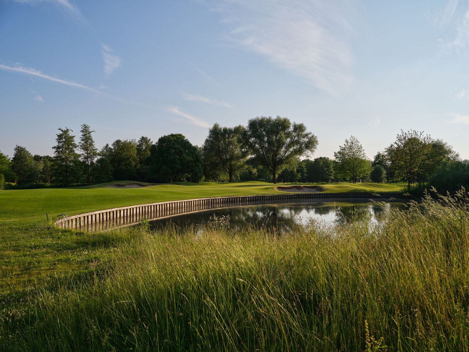 A scenic golf course featuring a wooden bridge over a tranquil pond surrounded by lush green fairways and trees.