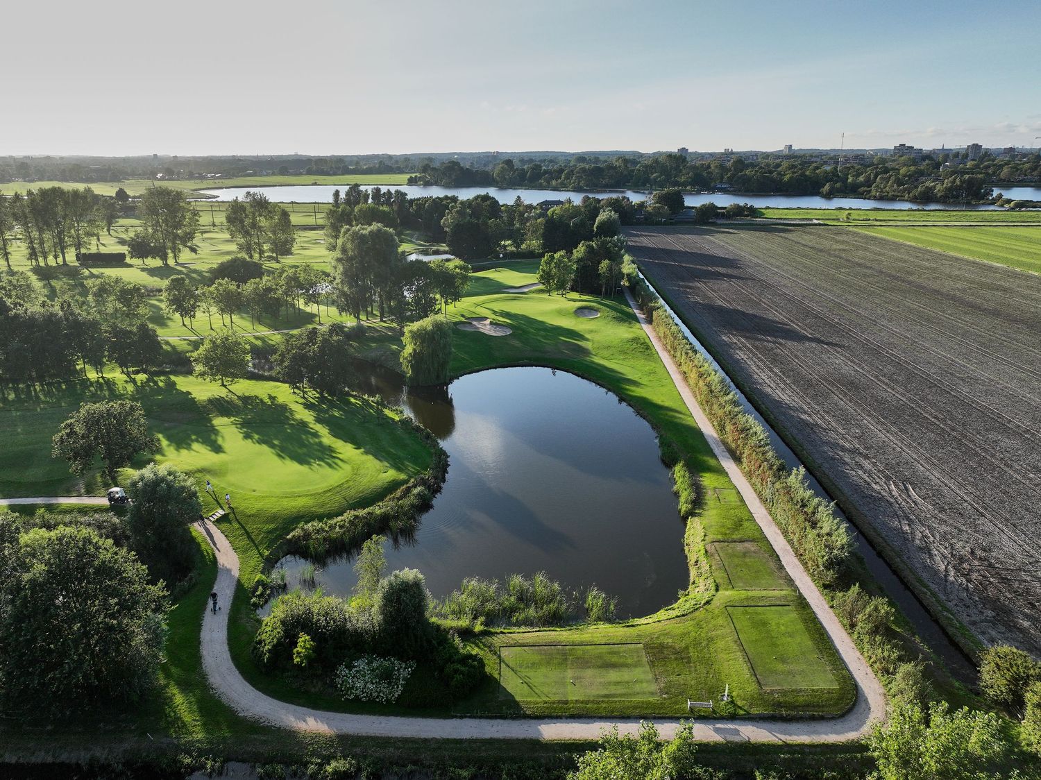 Aerial view of a peaceful golf course with a reflective pond surrounded by green fairways and agricultural fields.
