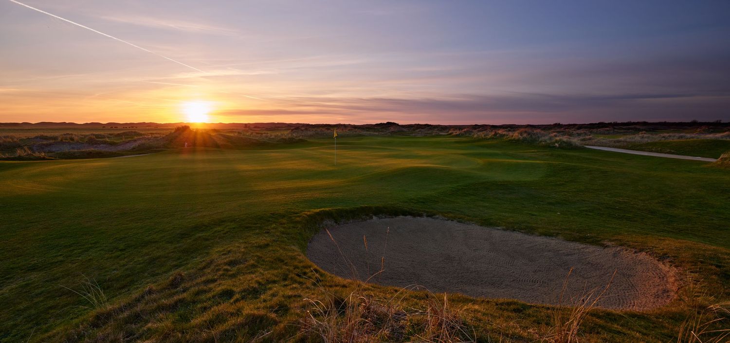A links golf course bunker and green glow in golden light during a breathtaking sunrise.