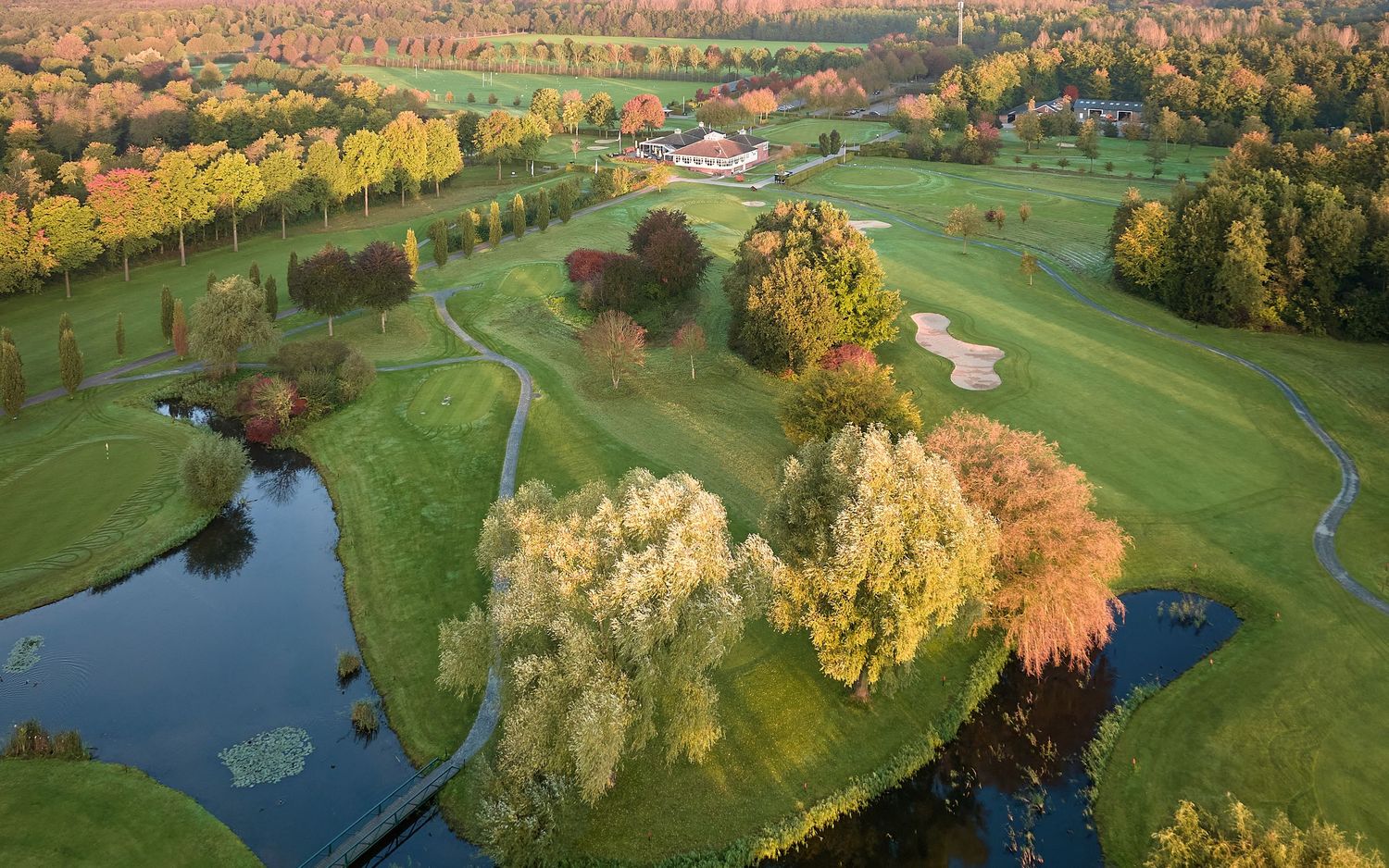 Aerial view of a golf course with winding water features and vibrant autumn trees.