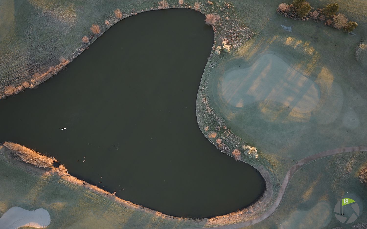 Aerial top-down view of a heart-shaped dark pond on a golf course fairway.