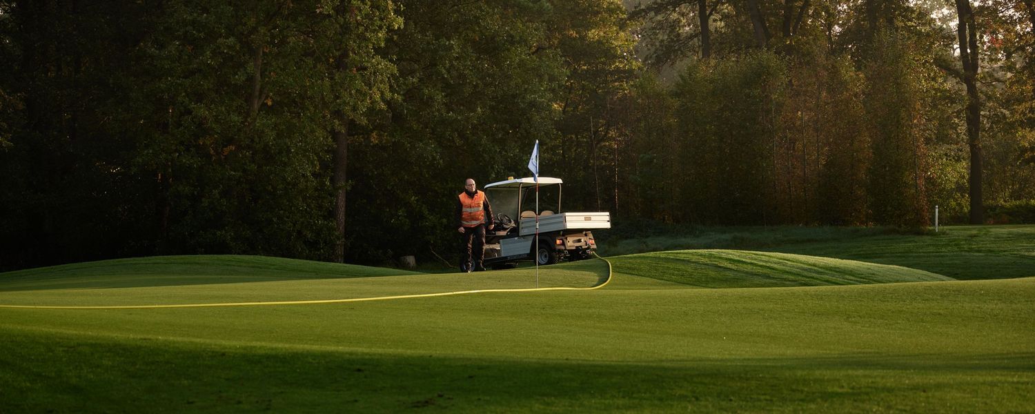 A groundskeeper operates maintenance equipment on a lush green golf course at dawn.