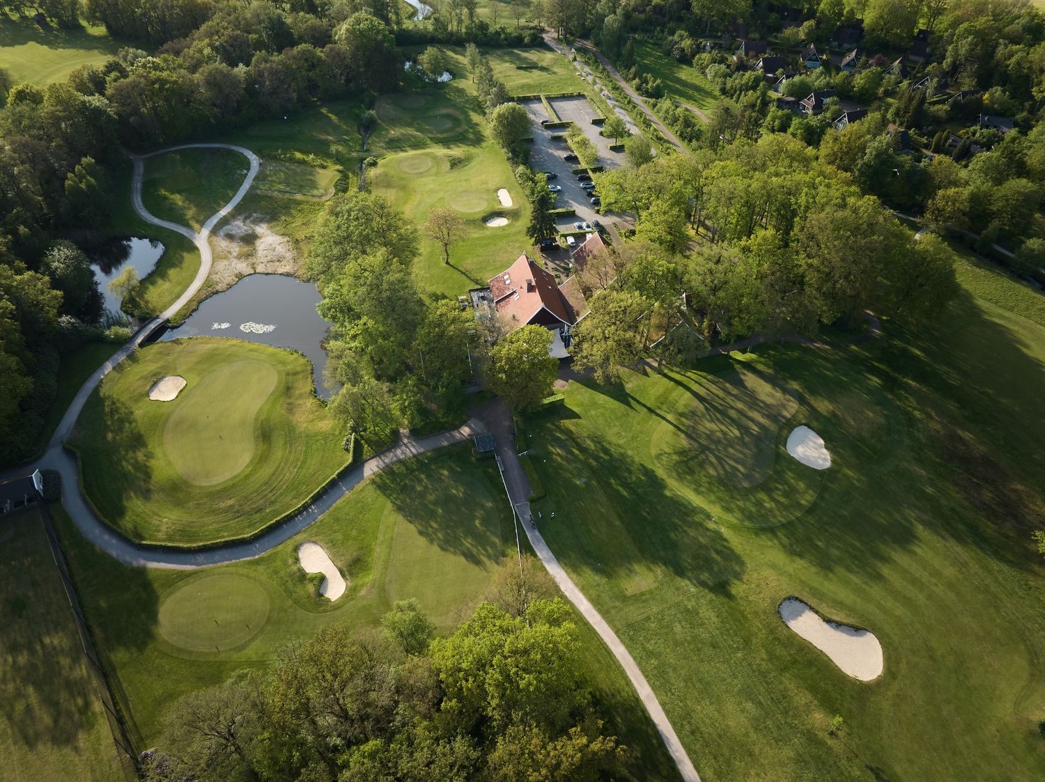 Aerial view of a golf course with pond, sand bunkers, clubhouse, and winding cart paths.